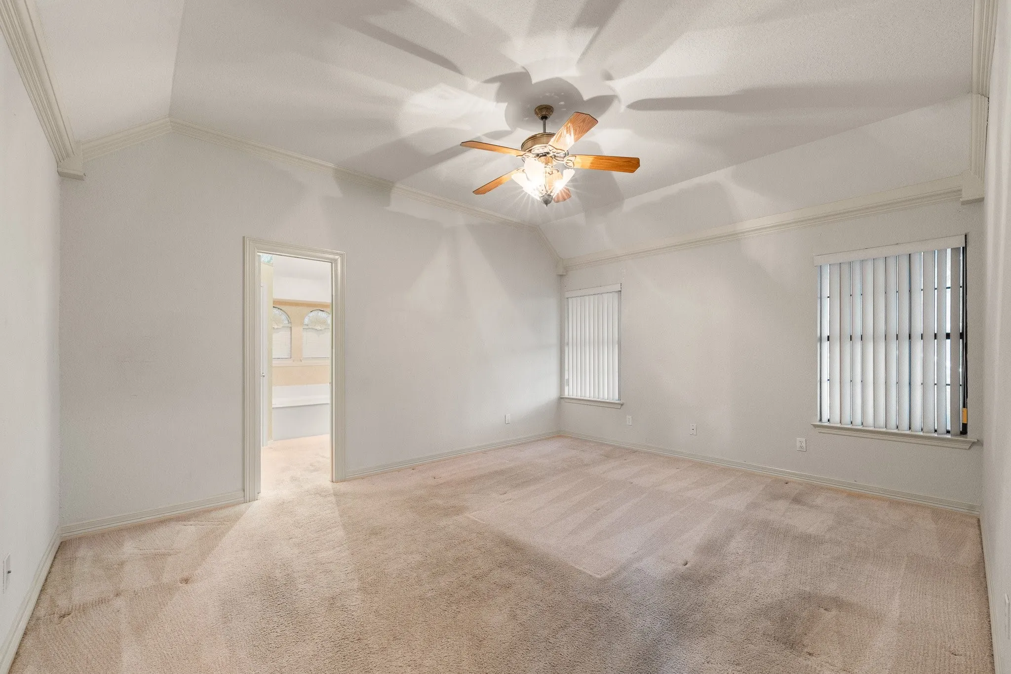 Spacious bedroom featuring vaulted ceilings, a ceiling fan with light fixture, two windows with vertical blinds, and neutral-toned carpet