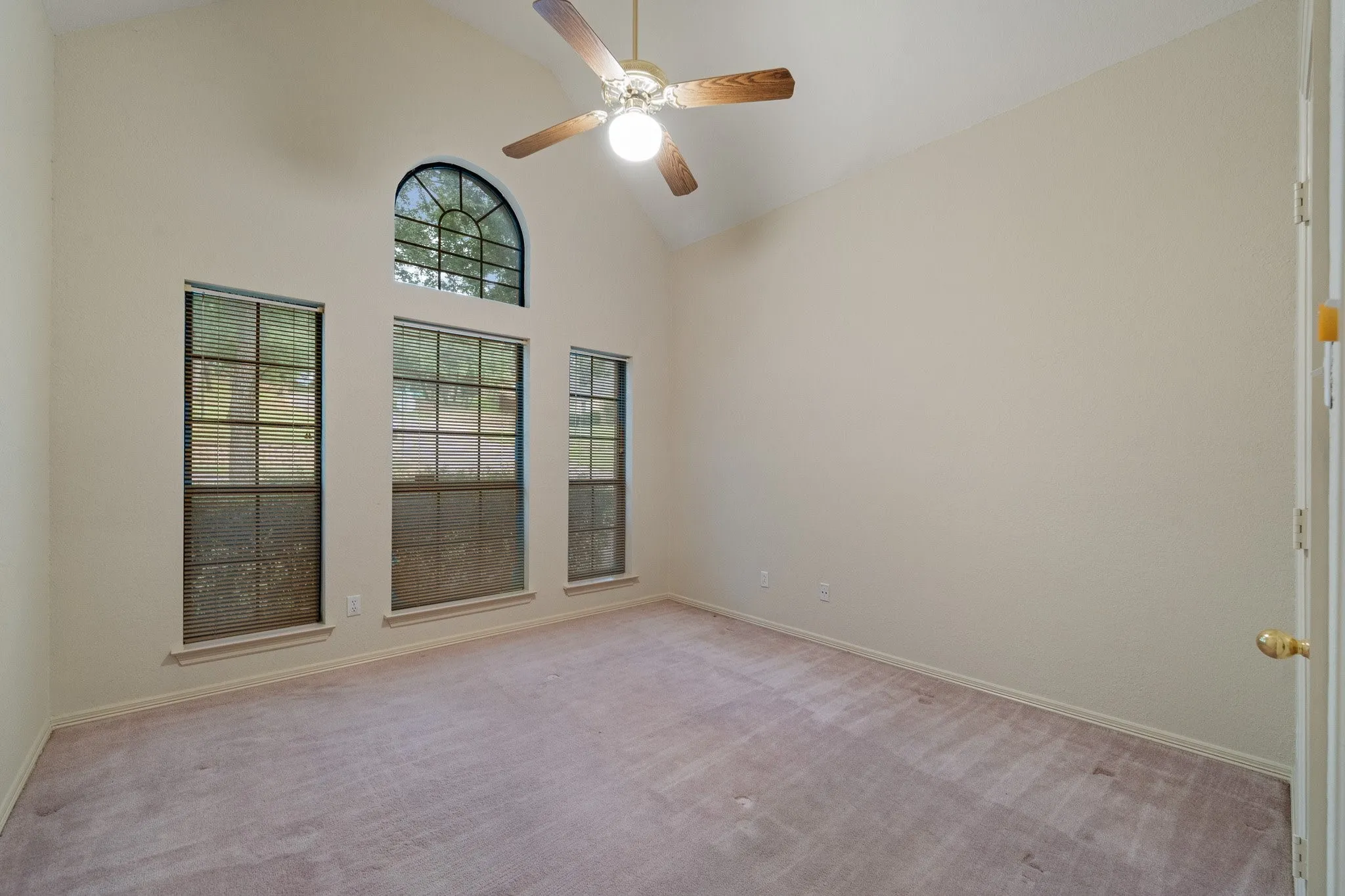 Vaulted ceiling room featuring an arched window, two vertical windows, and a ceiling fan with integrated lighting