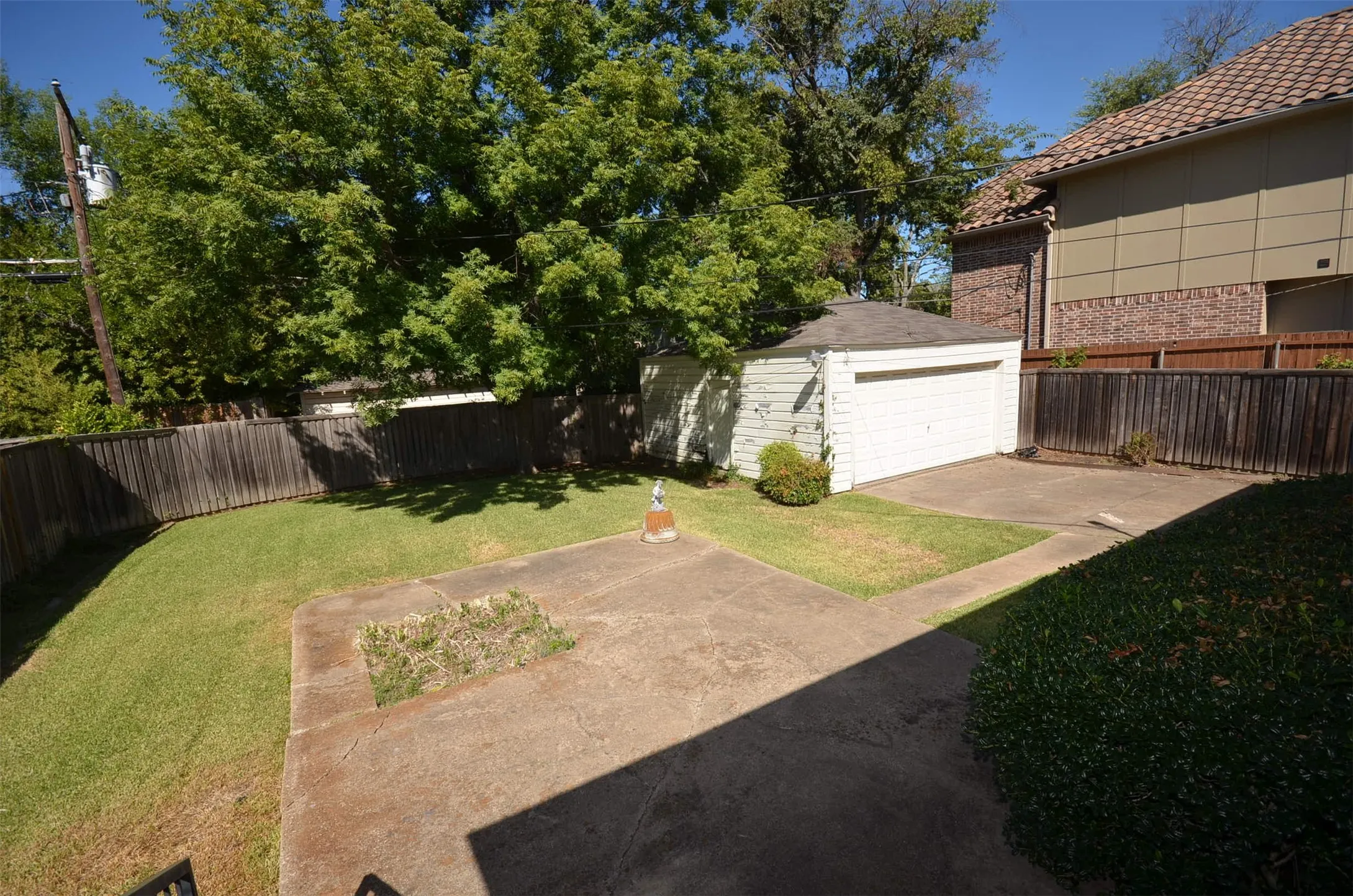 Expansive backyard space featuring a concrete patio, a detached garage with a white overhead door, and a wooden privacy fence