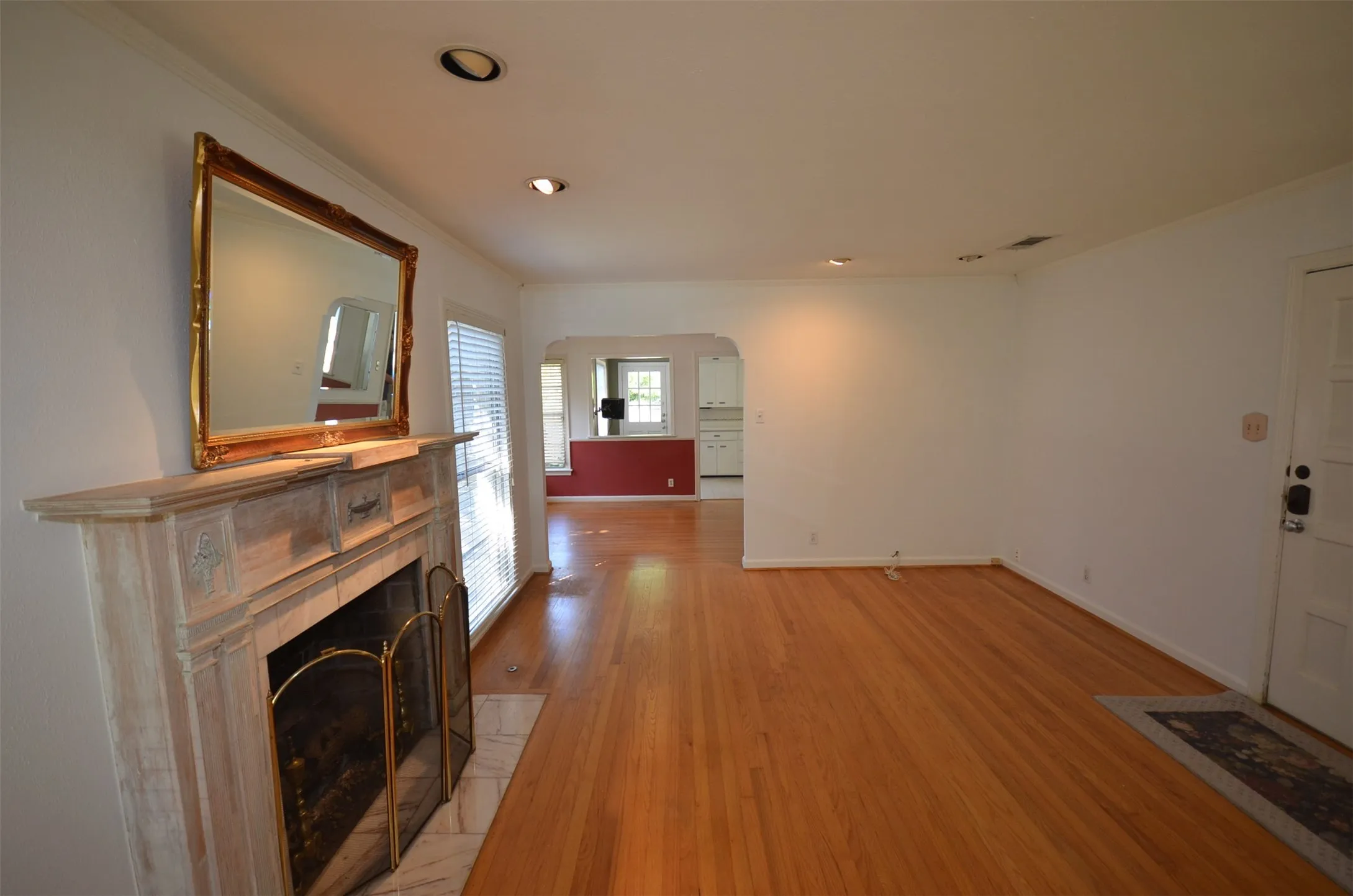 Living space featuring wood-finish flooring, a decorative fireplace with a mantel, recessed lighting, white interior walls, and an arched entry to an additional room