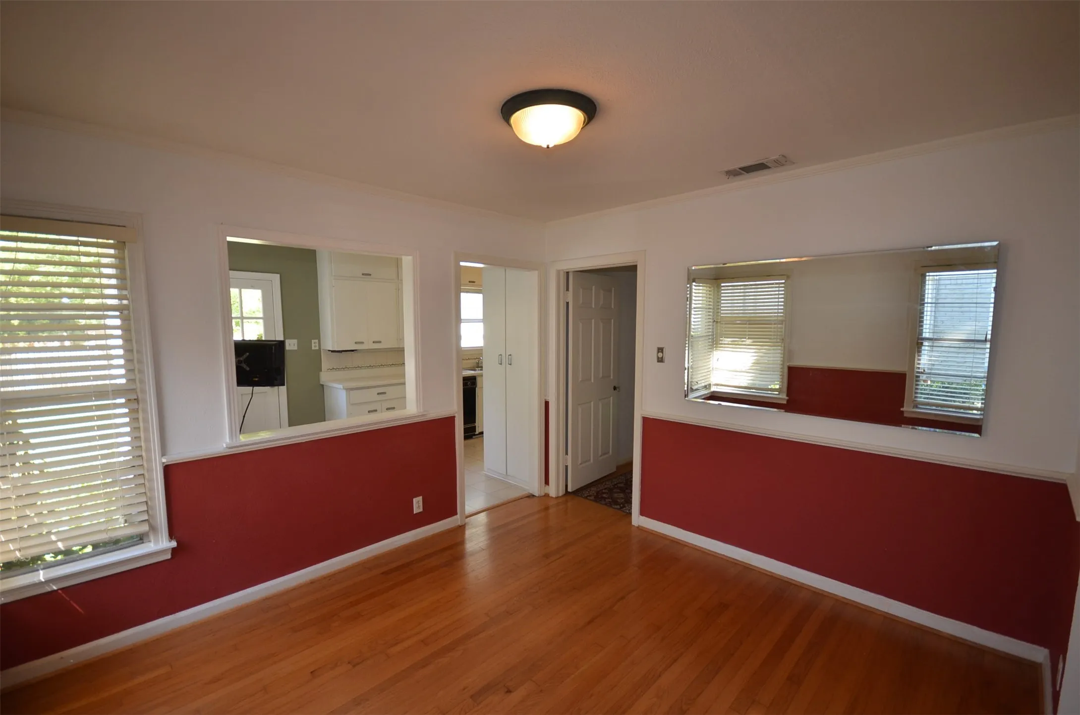 Hardwood flooring throughout, featuring a pass-through opening to the kitchen, a built-in wall mirror, and privacy blinds on windows