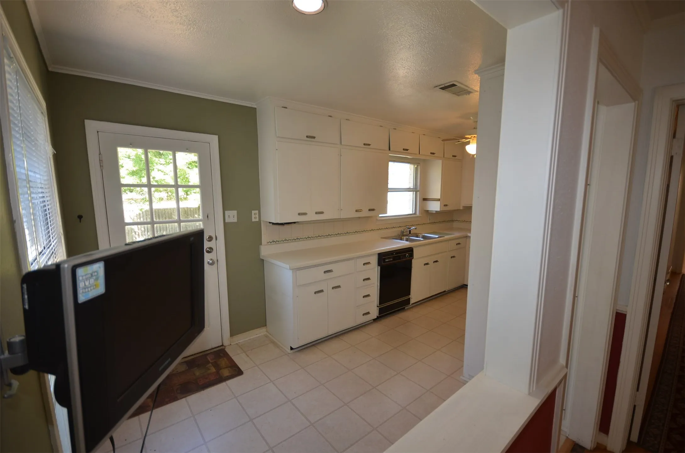 Kitchen featuring white cabinetry, light-toned countertops, a black built-in dishwasher, and a window above the sink