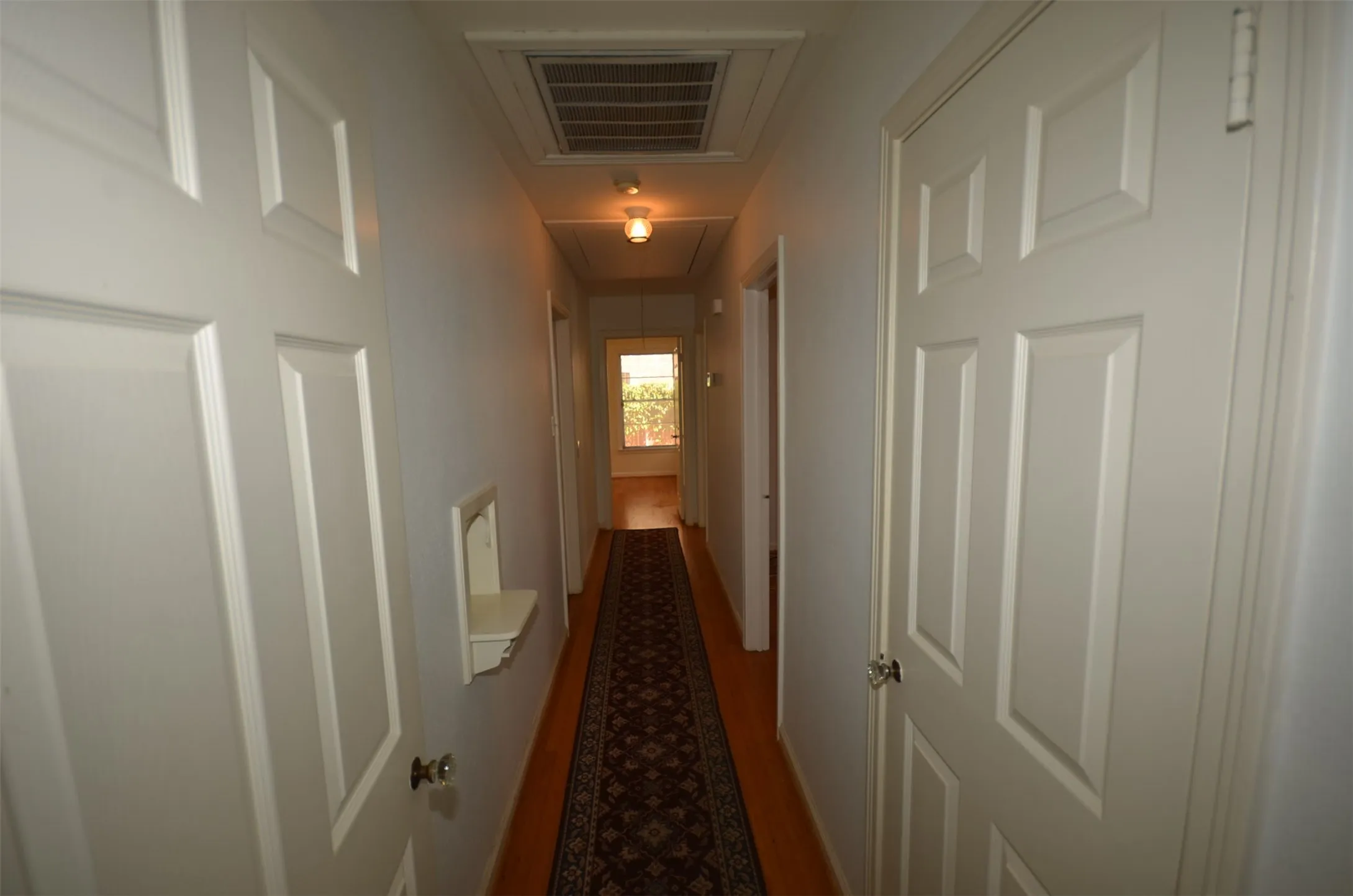 Hallway featuring wood-finish flooring, white paneled doors, and ceiling-mounted light fixtures