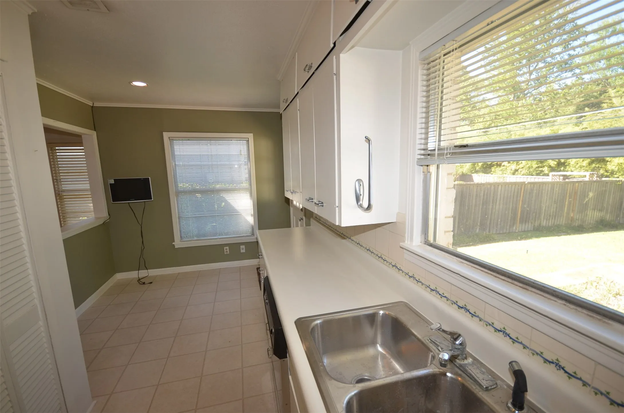 Kitchen space featuring a double basin stainless steel sink, white cabinetry, and light-toned tile flooring