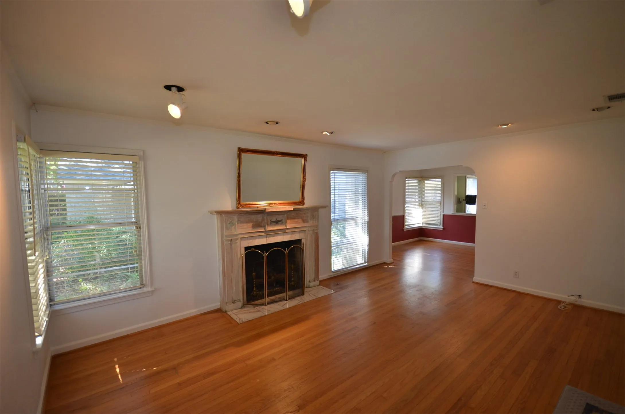 Living area featuring wood-finish flooring, a decorative fireplace with a stone-surround mantel, white walls, and track lighting