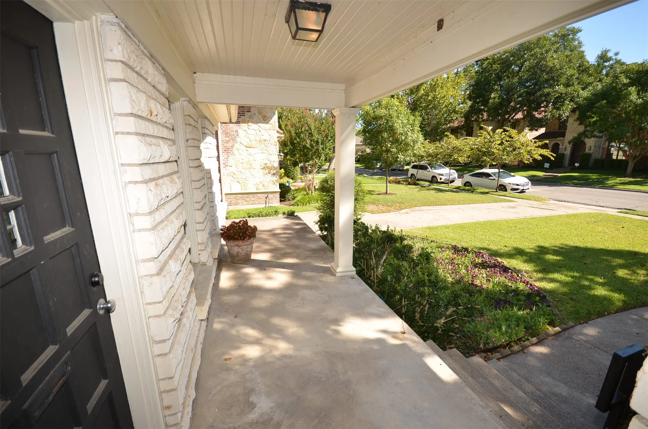 Covered front porch featuring a black paneled entry door, white brick facade, concrete flooring, and a beadboard ceiling