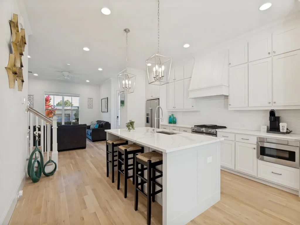 Open-concept kitchen featuring an oversized island with seating, white shaker cabinetry, stainless steel appliances, and wood-finish flooring throughout