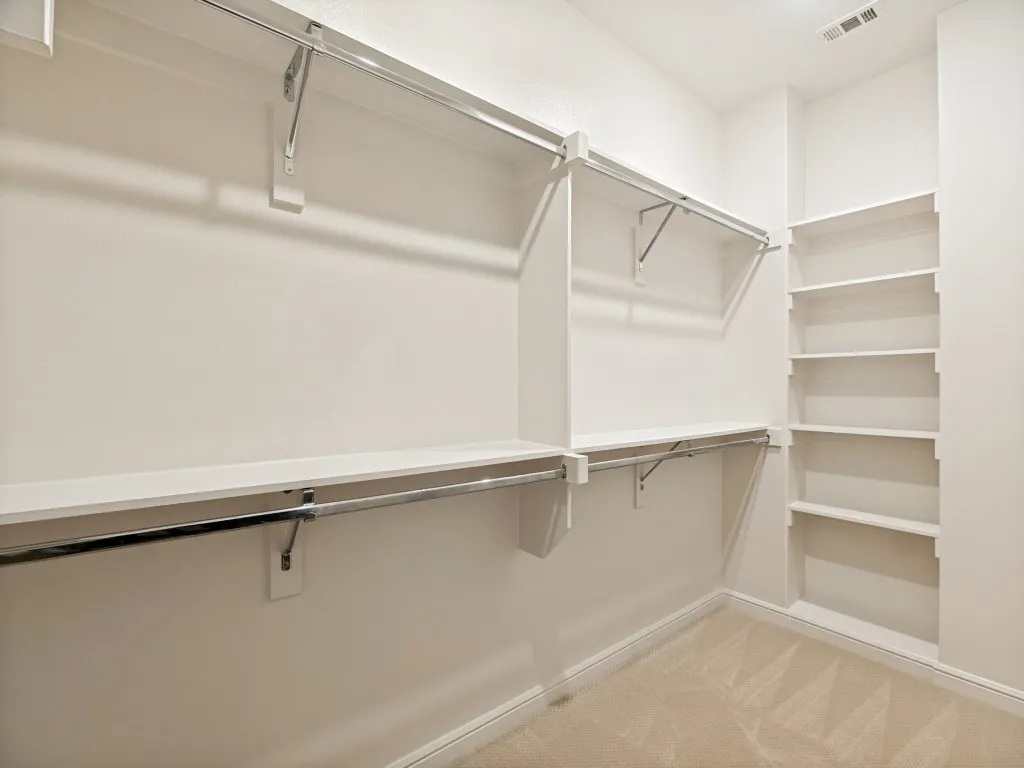 Walk-in closet featuring built-in shelving, multiple hanging rods, and neutral-toned carpeting