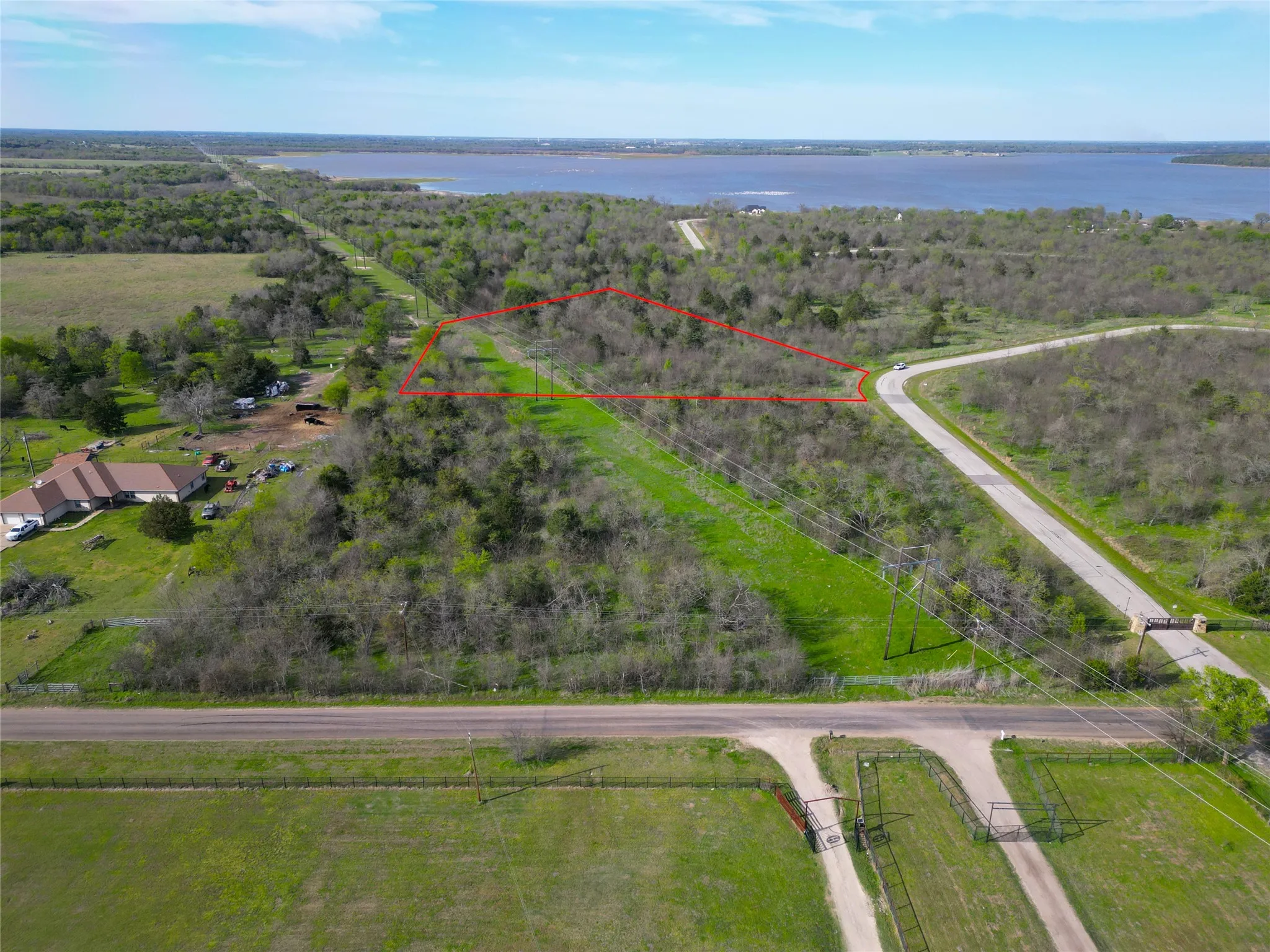 Expansive undeveloped land parcel featuring a natural tree line, a cleared area with grass, direct road frontage, and proximity to a body of water