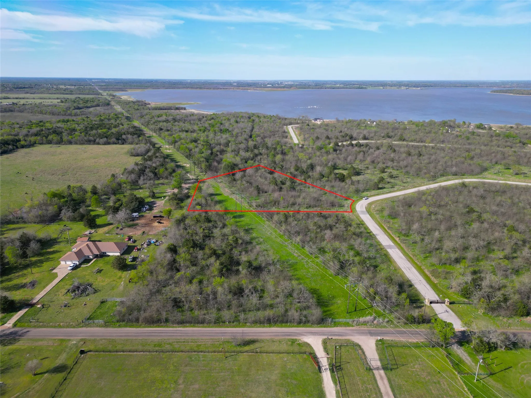 Expansive undeveloped land parcel outlined in red, featuring mature trees and a clear lake visible in the background