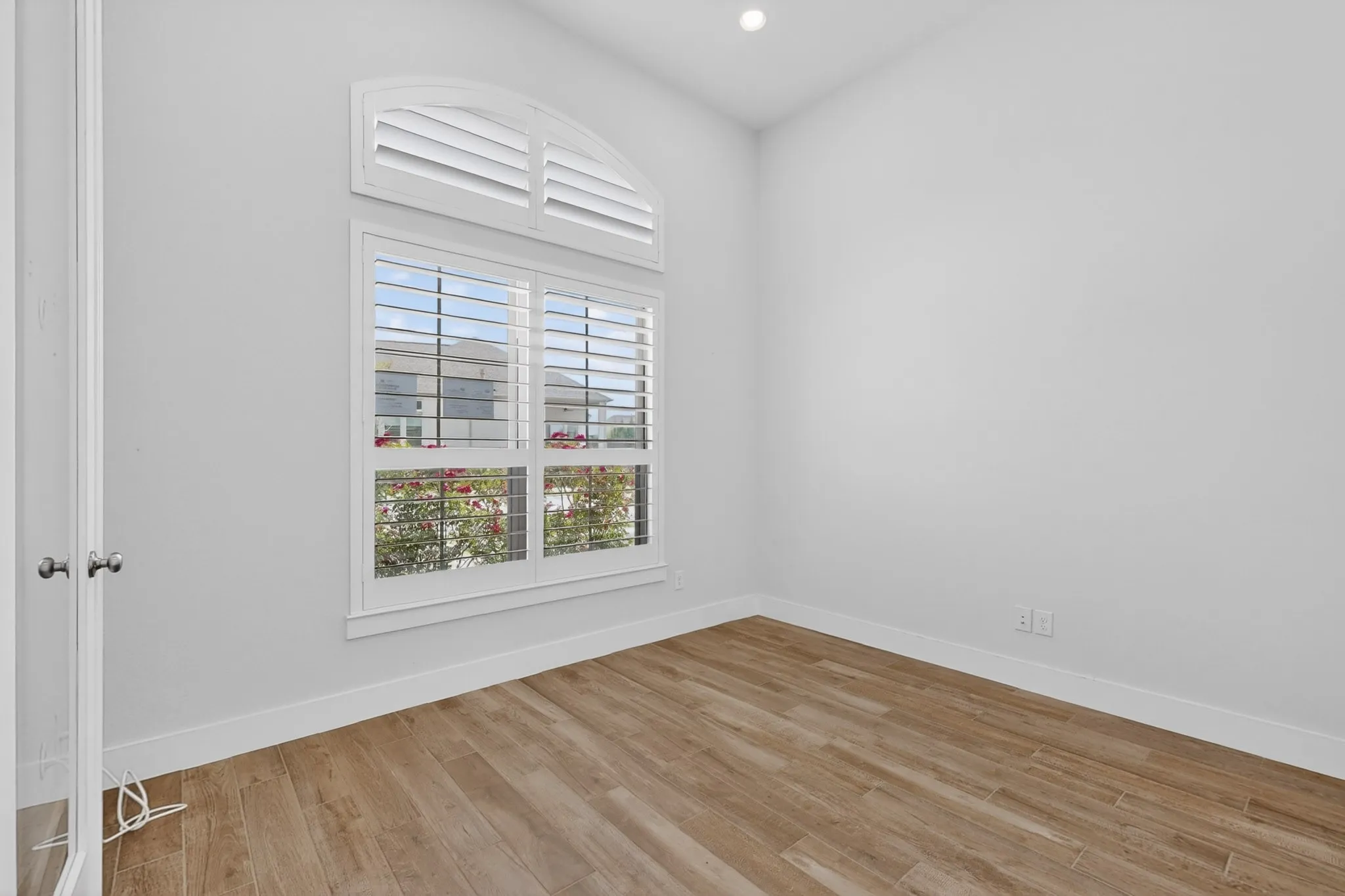 Room featuring a large arched window with white plantation shutters, wood-finish flooring, recessed lighting, and a neutral wall color