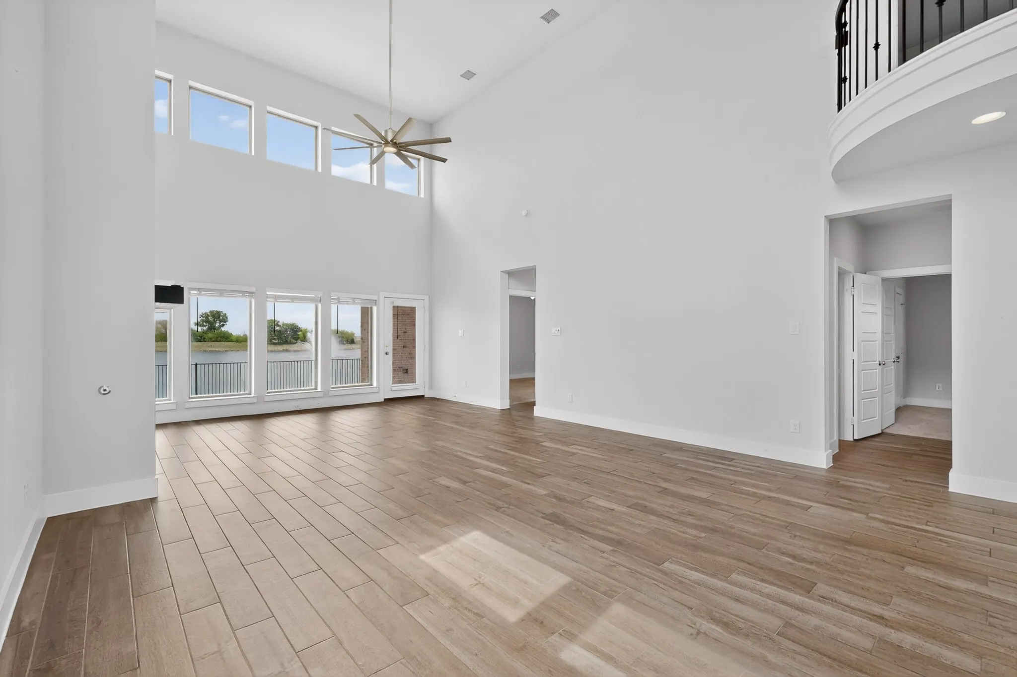 Two-story living area featuring wood-finish flooring, a contemporary ceiling fan, and a wall of windows