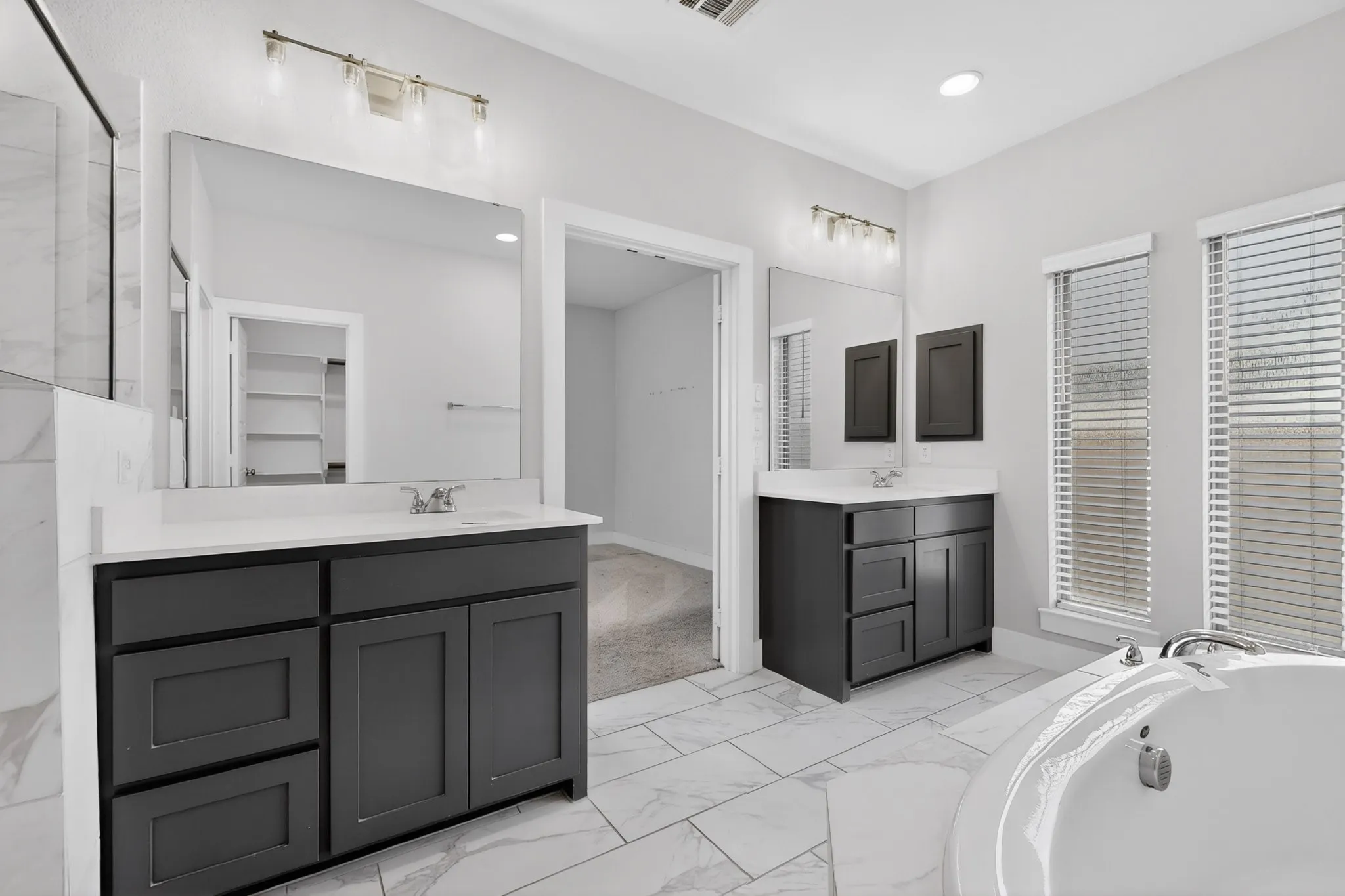 Dual vanities with dark cabinetry and light countertops, a built-in soaking tub, and tiled flooring