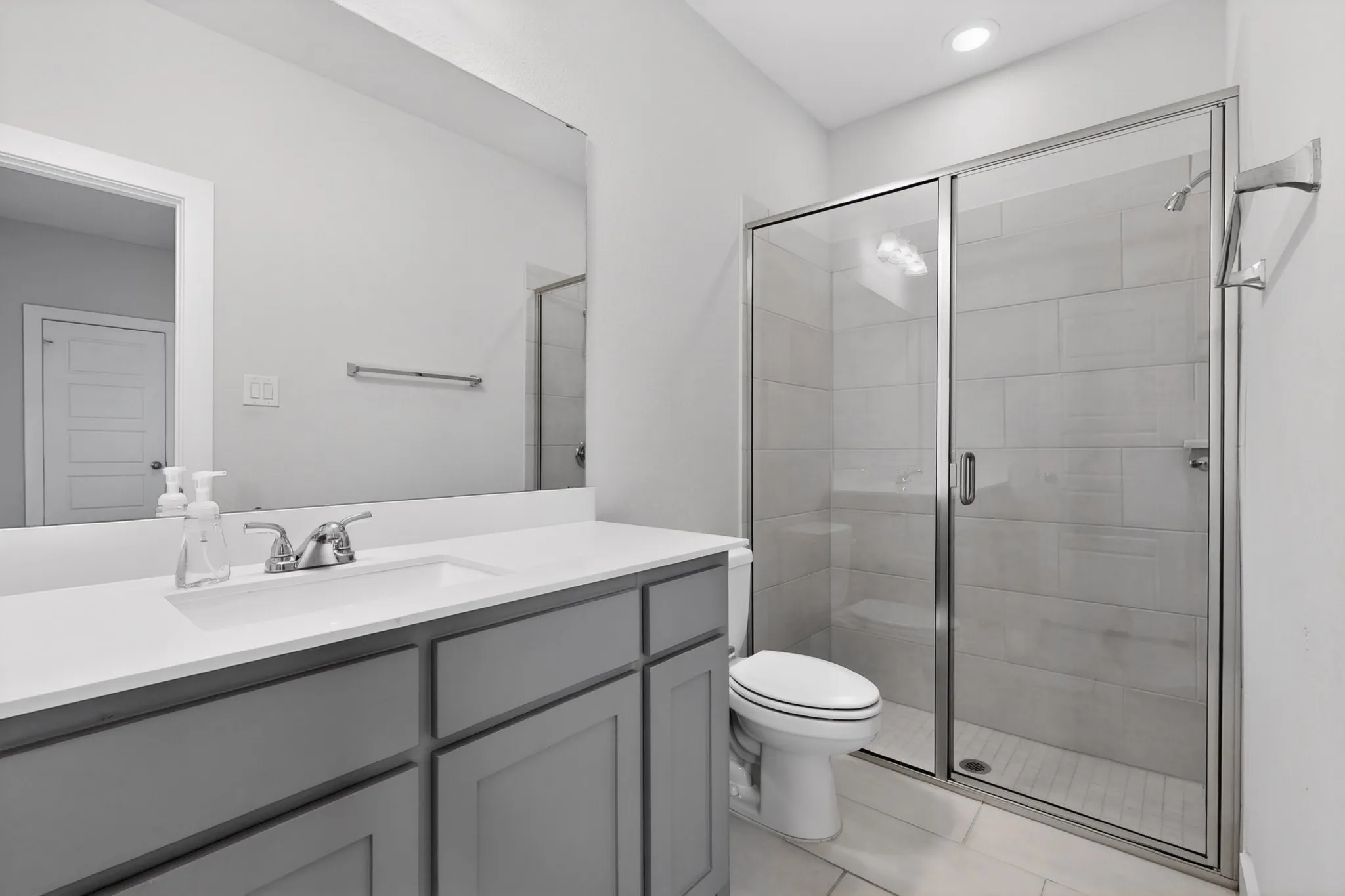 Contemporary bathroom featuring a glass-enclosed shower with tile surround, a single vanity with a white countertop and undermount sink, and recessed lighting