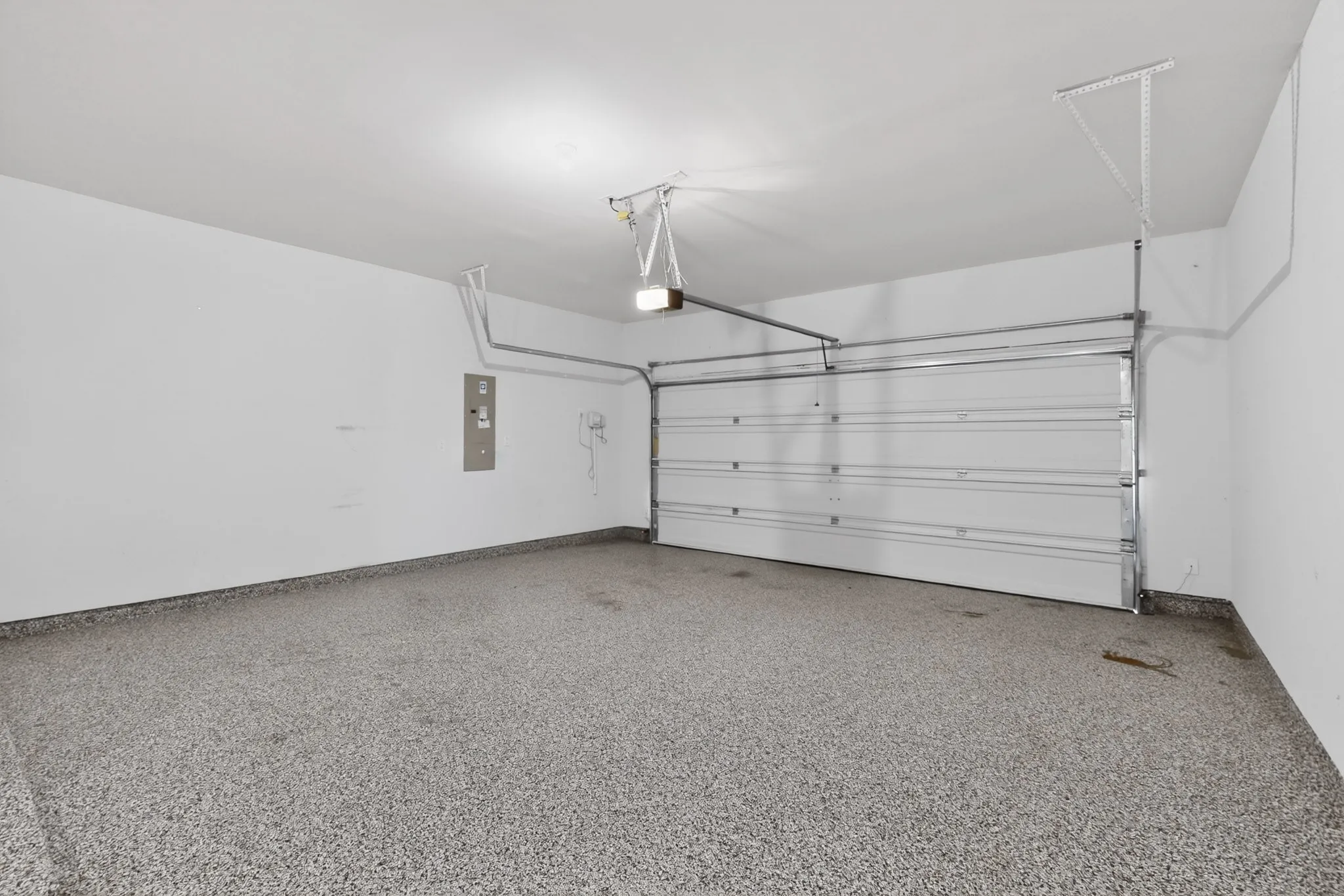 Spacious garage featuring a speckled epoxy floor coating, white walls, and an overhead garage door opener mechanism