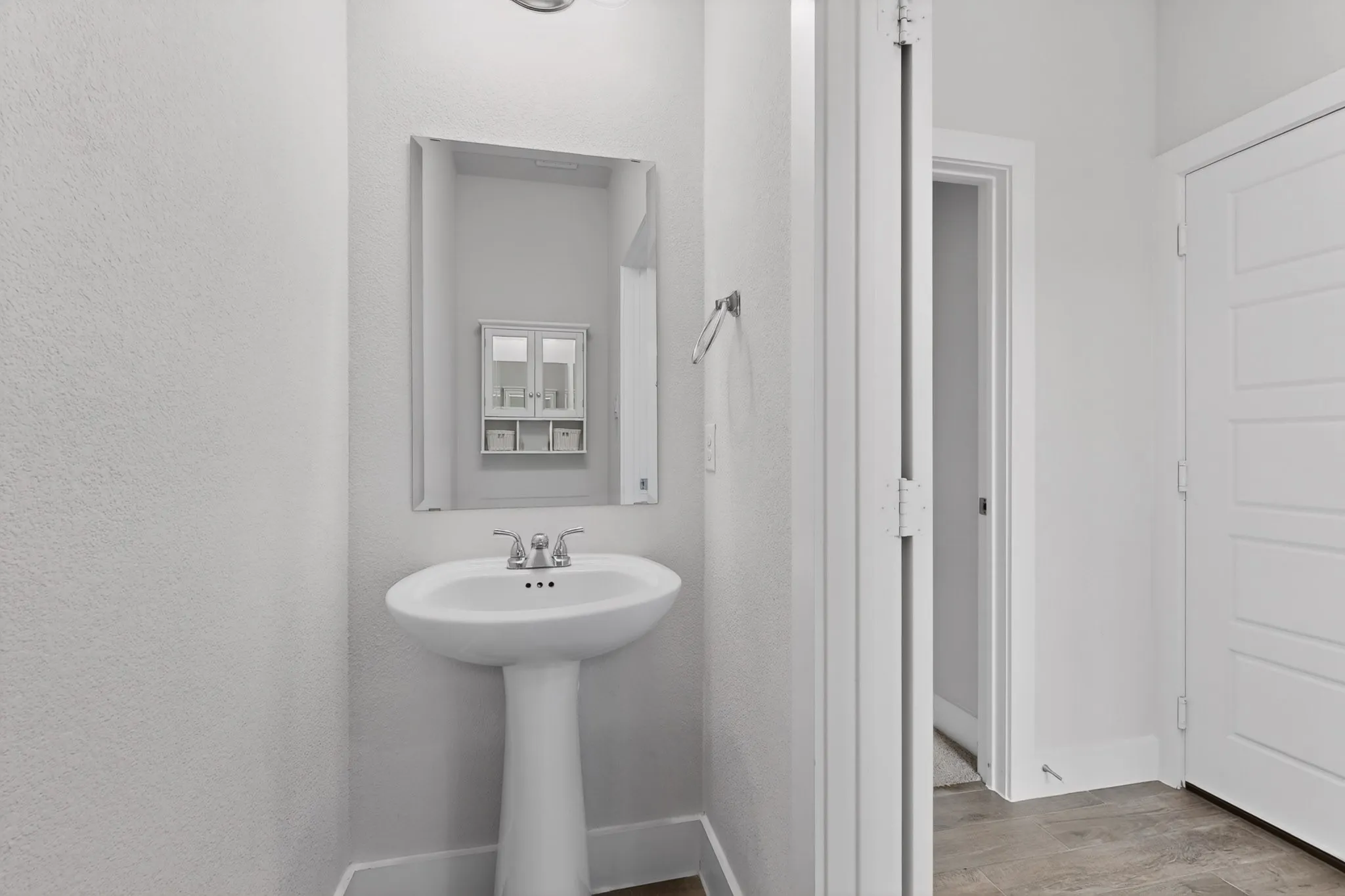 Pedestal sink with chrome faucet, framed mirror, and a wall-mounted towel bar