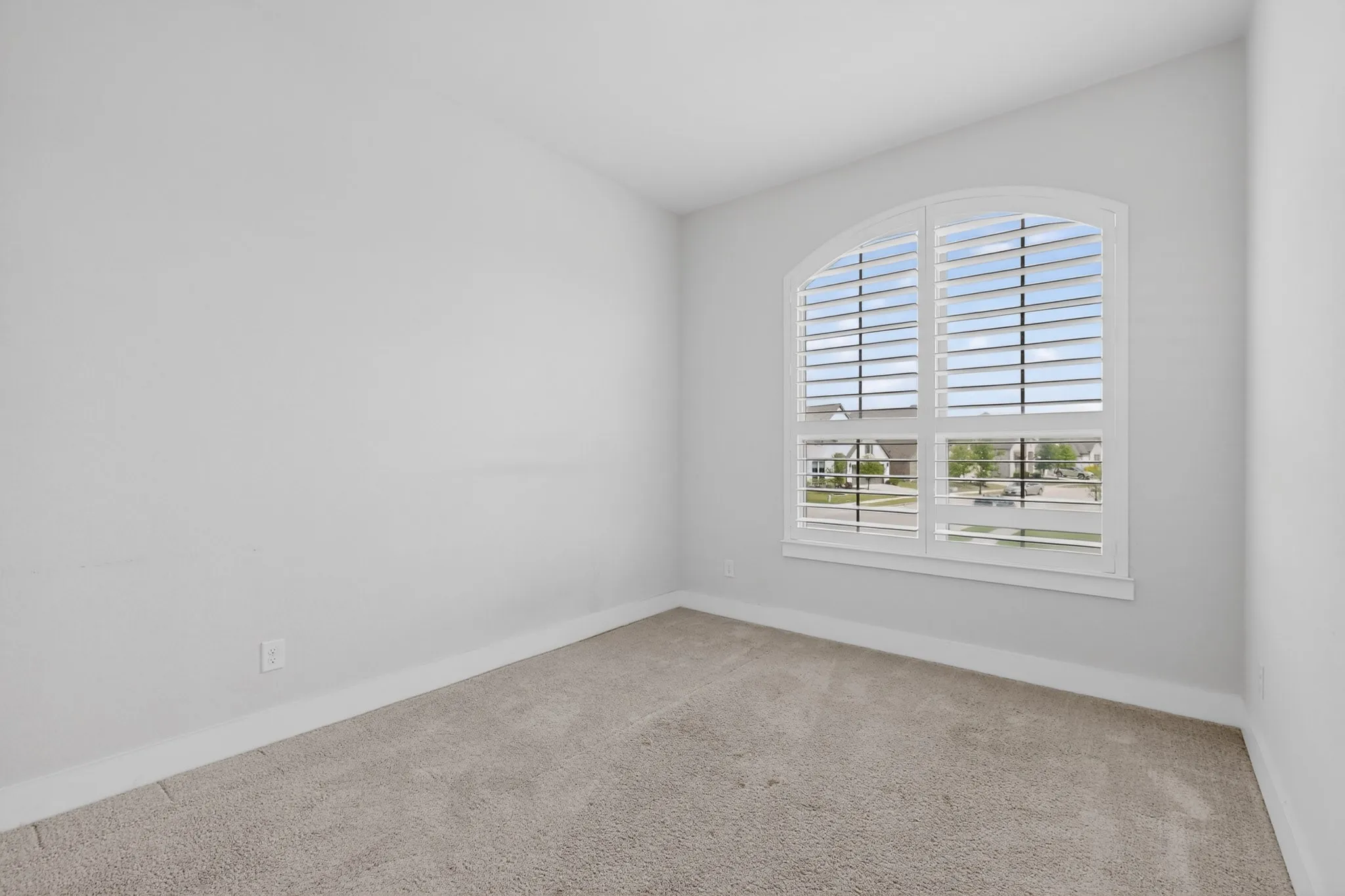 Light gray walls with white trim, arched window with plantation shutters, light-colored carpet flooring