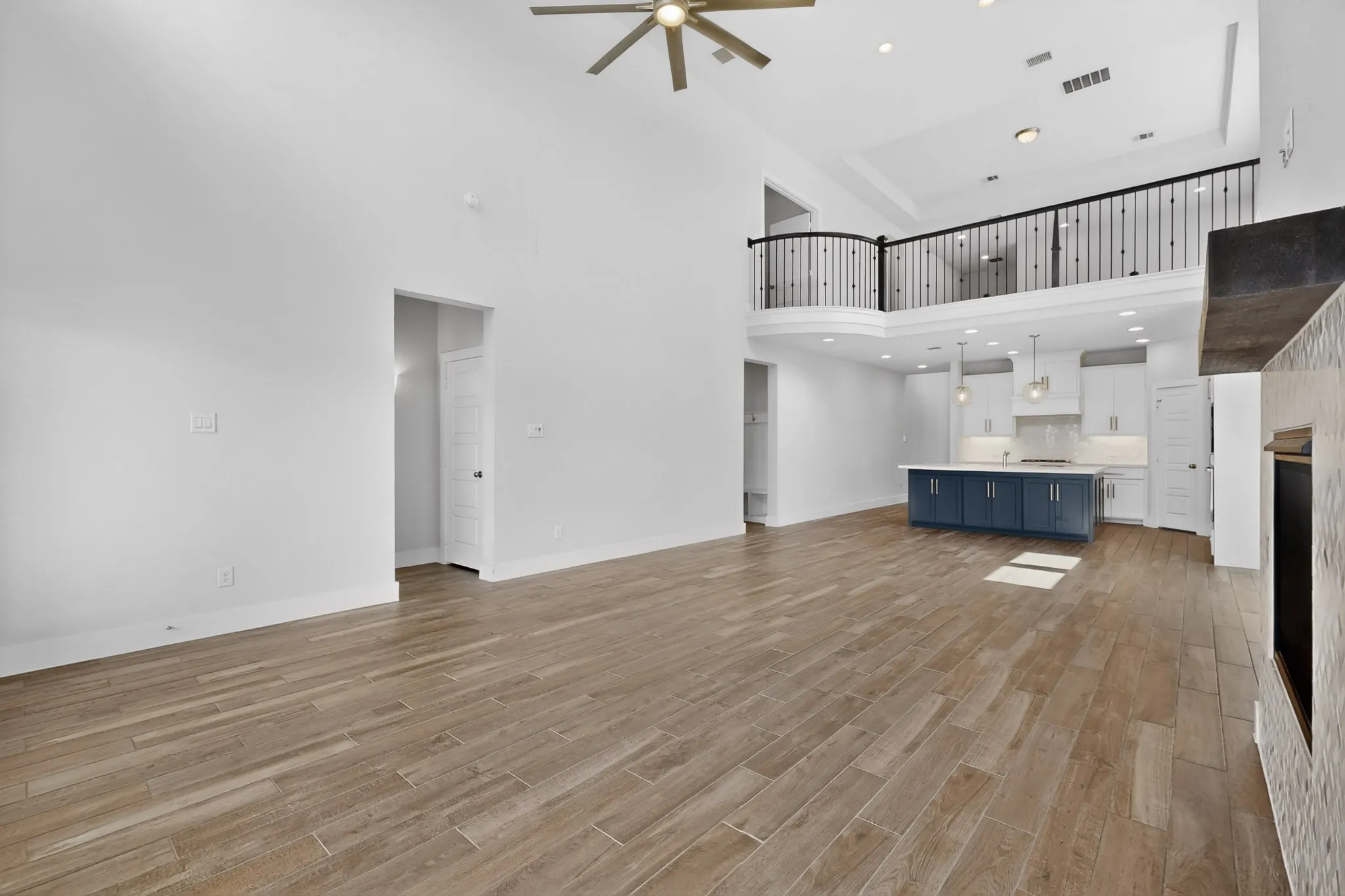 Spacious open-concept living area featuring high ceilings, wood-finish flooring, and a contemporary ceiling fan