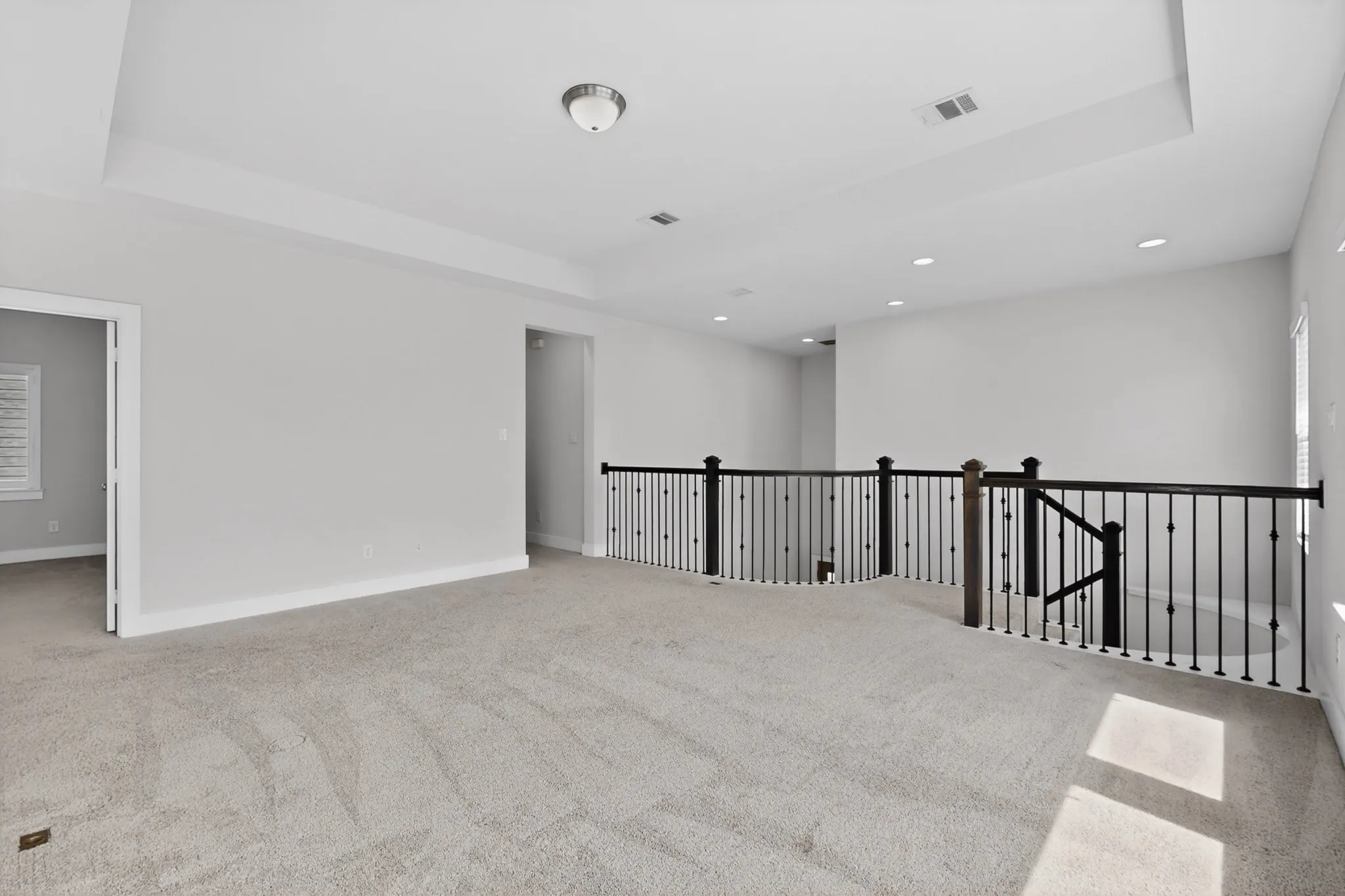 Spacious carpeted landing featuring a tray ceiling, recessed lighting, and a dark iron spindle railing with wood newel posts