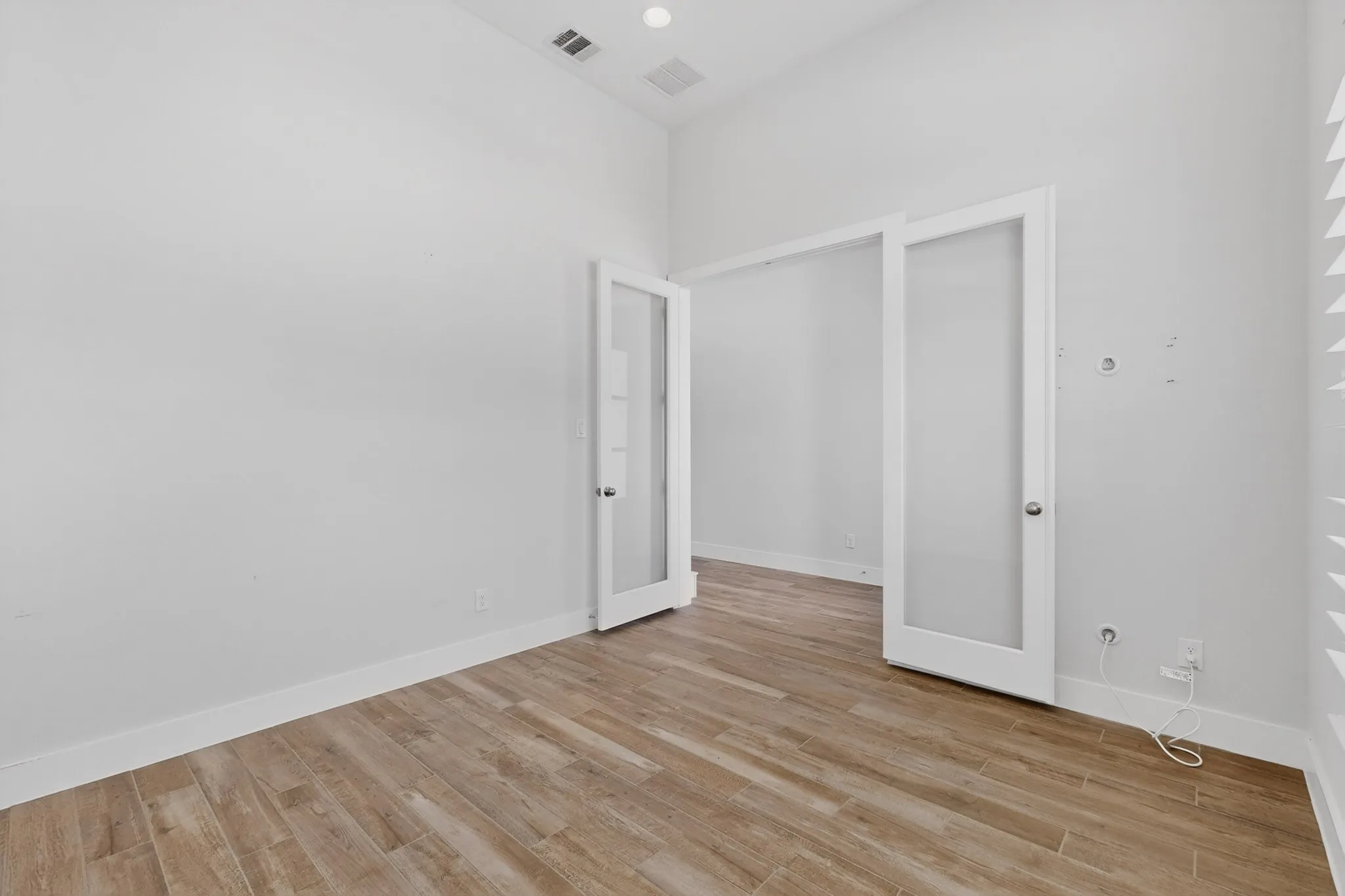 Bright room featuring wood-finish flooring, white baseboards, and double French doors with frosted glass panels