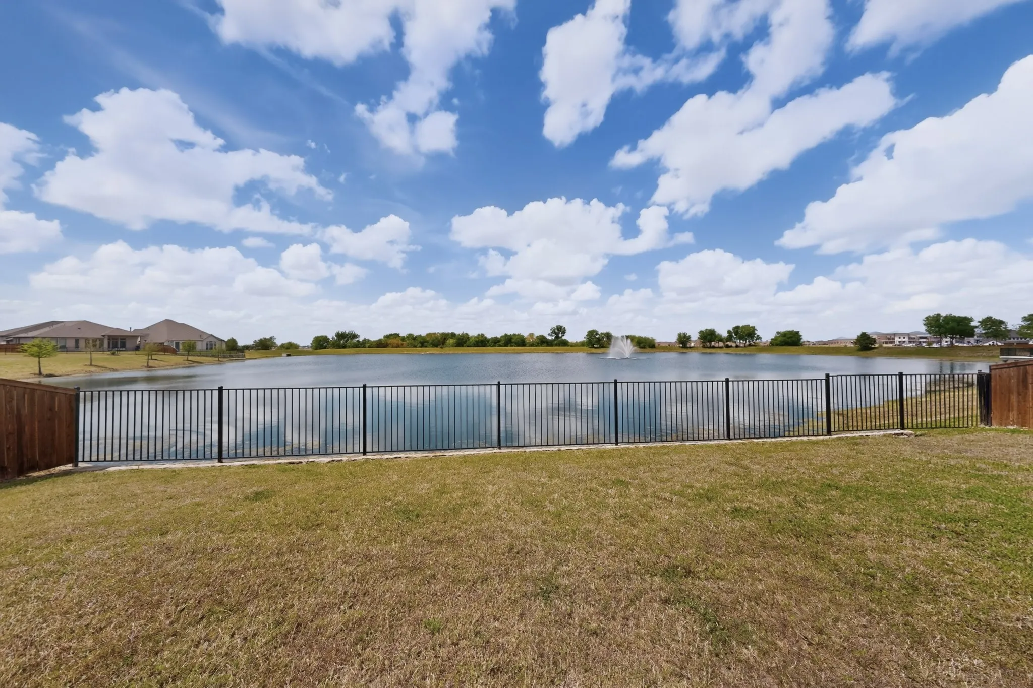 Expansive green lawn with a black metal fence bordering a serene body of water