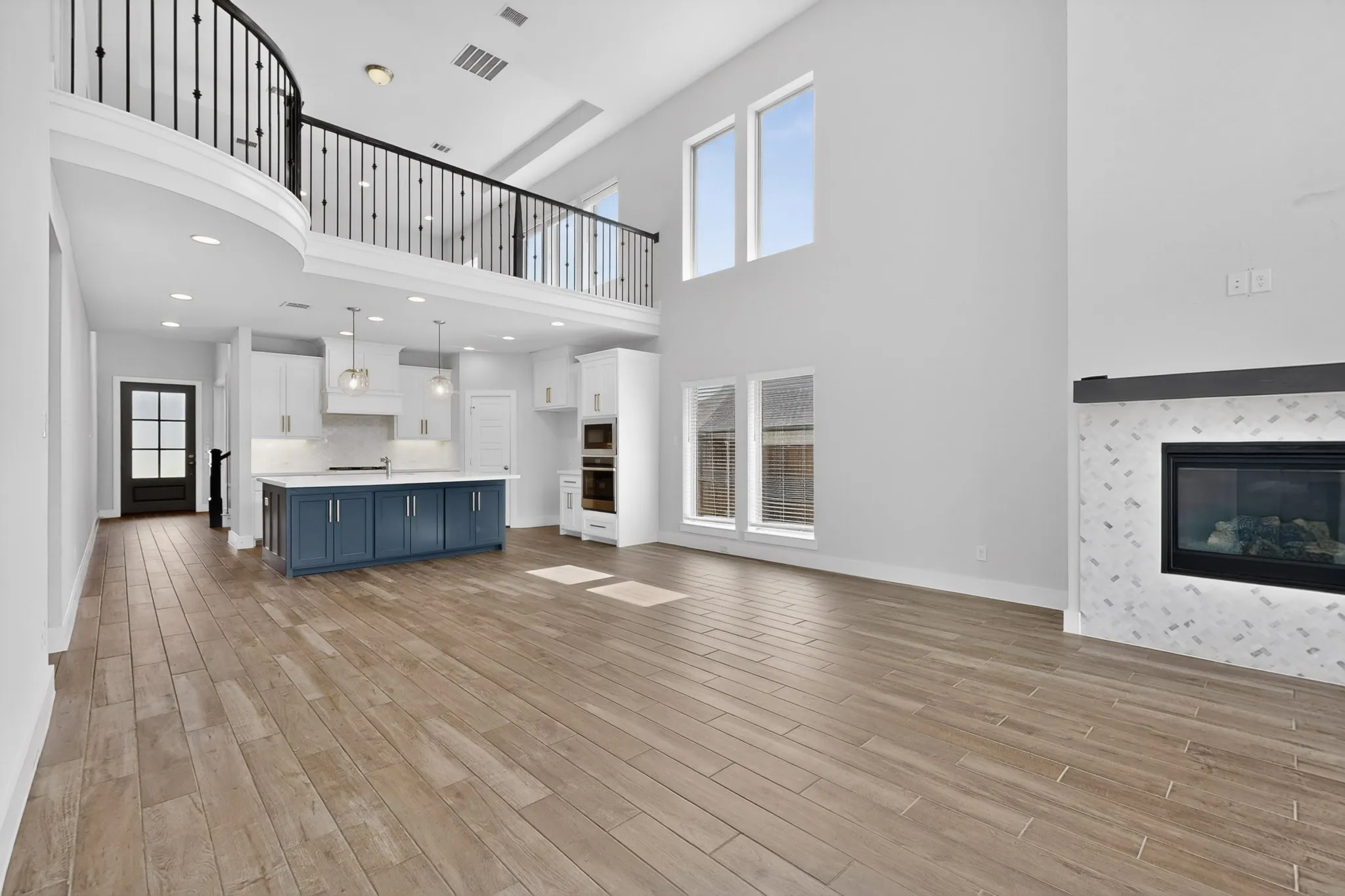 Open-concept living area featuring high ceilings, wood-finish flooring, and a fireplace with a decorative tile surround and dark mantel