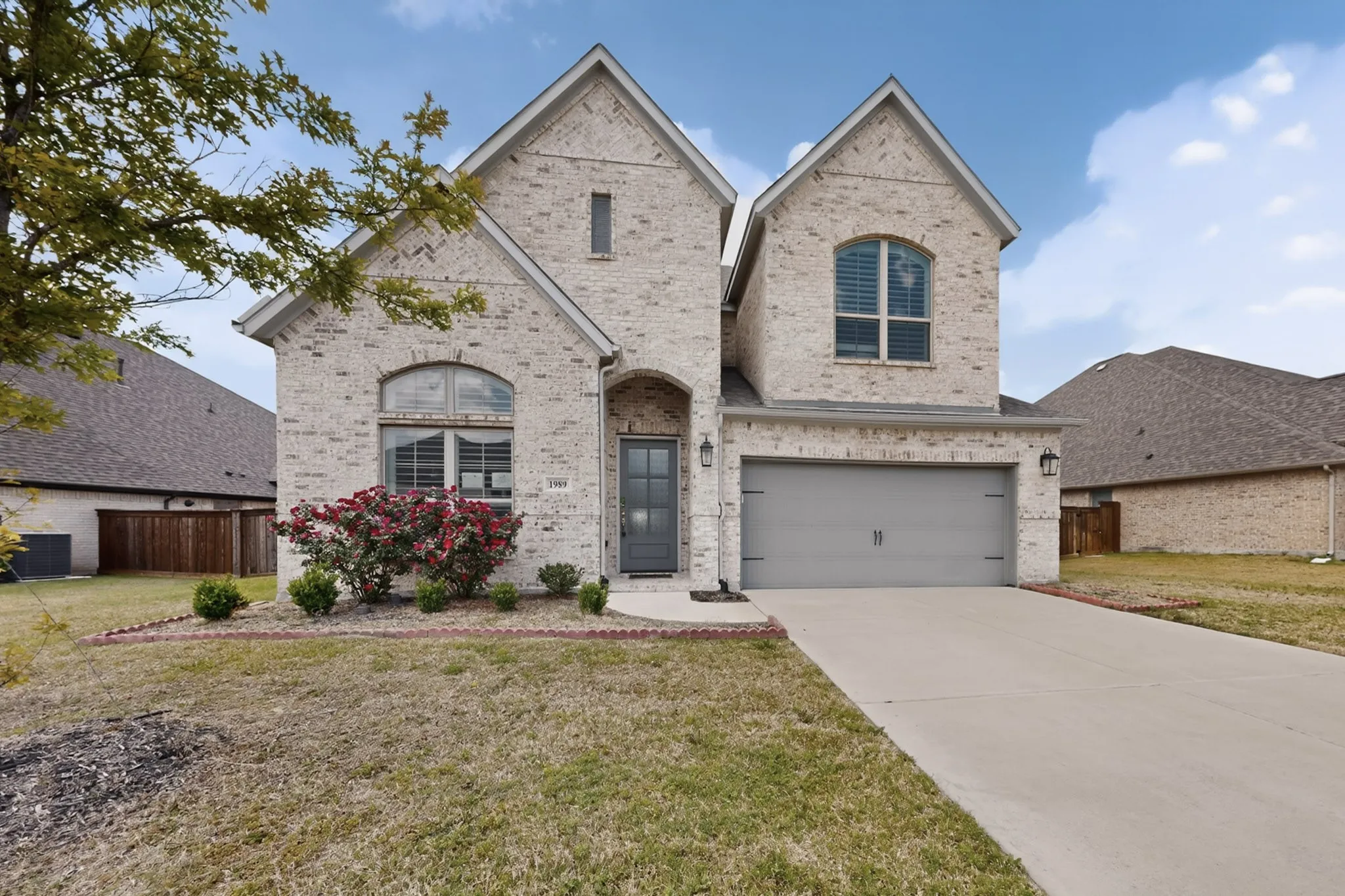 Light-colored brick exterior featuring a multi-gable roofline, an arched entry, a dark gray front door, and a two-car garage with a matching dark gray door