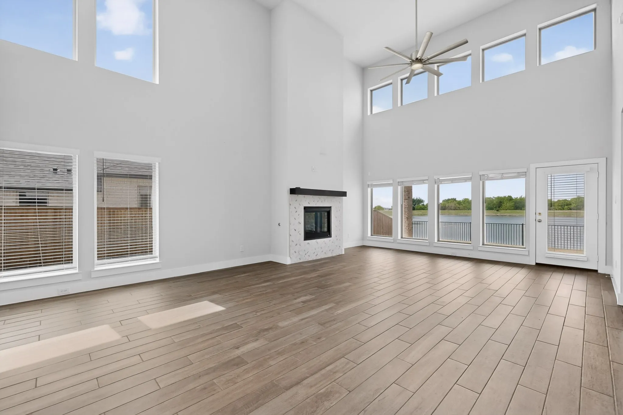 Two-story living area featuring wood-finish flooring, a contemporary fireplace with a tiled surround and dark mantel, and a ceiling fan