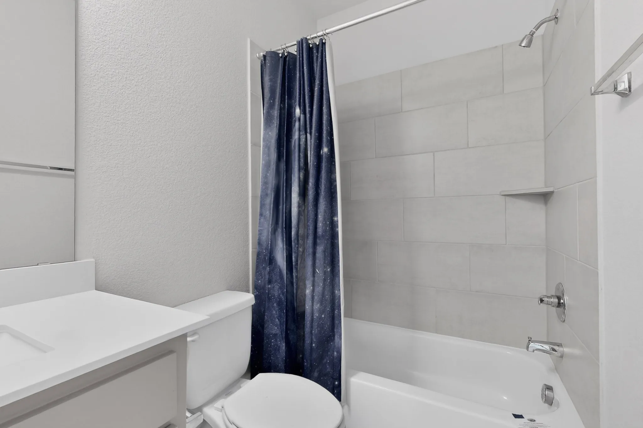 Bathroom featuring a white vanity with integrated sink, white toilet, and a tiled shower-over-tub combination with a built-in shelf