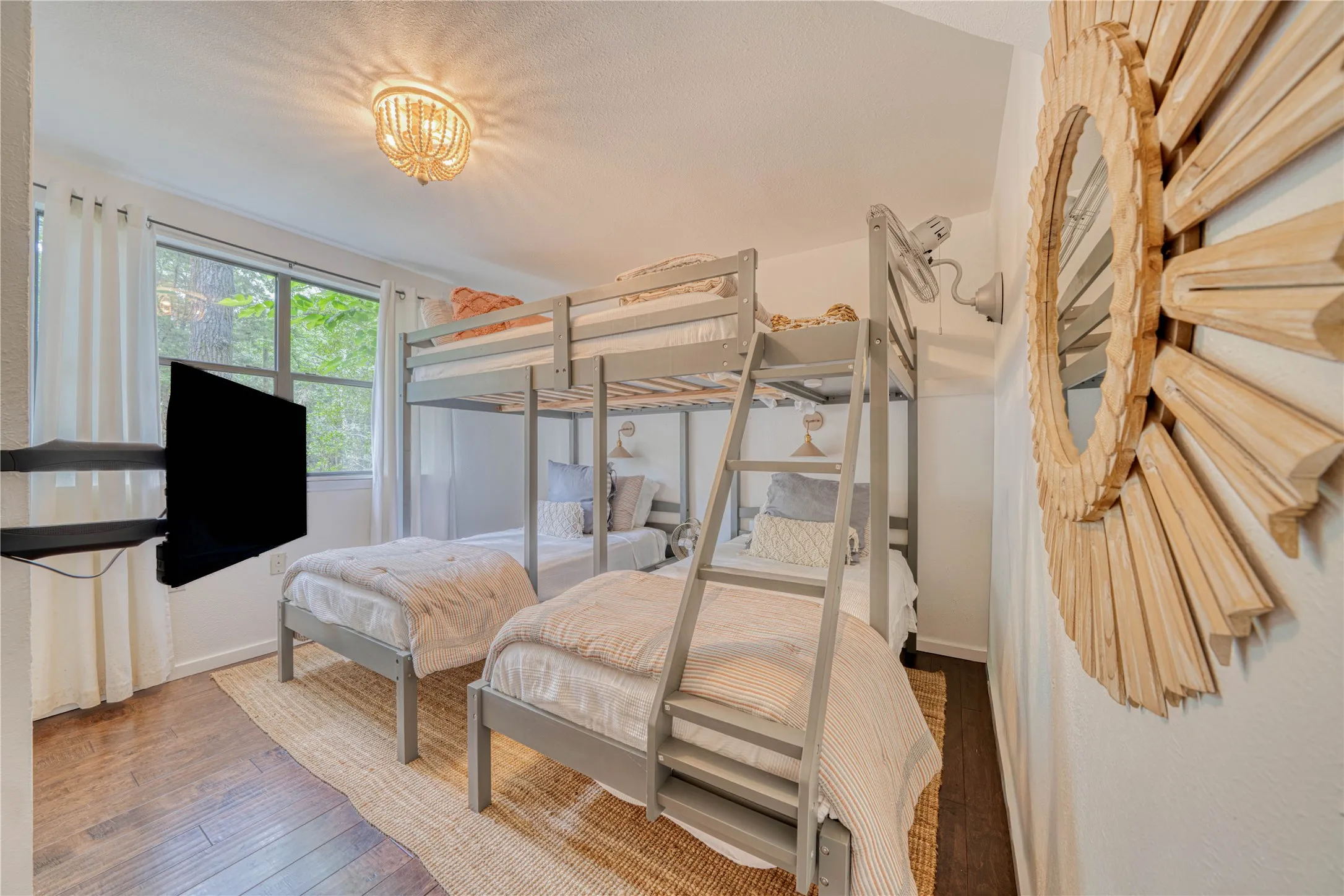 Bedroom featuring wood-finish flooring, a window with white curtains, a ceiling-mounted light fixture, and a wall-mounted sconce