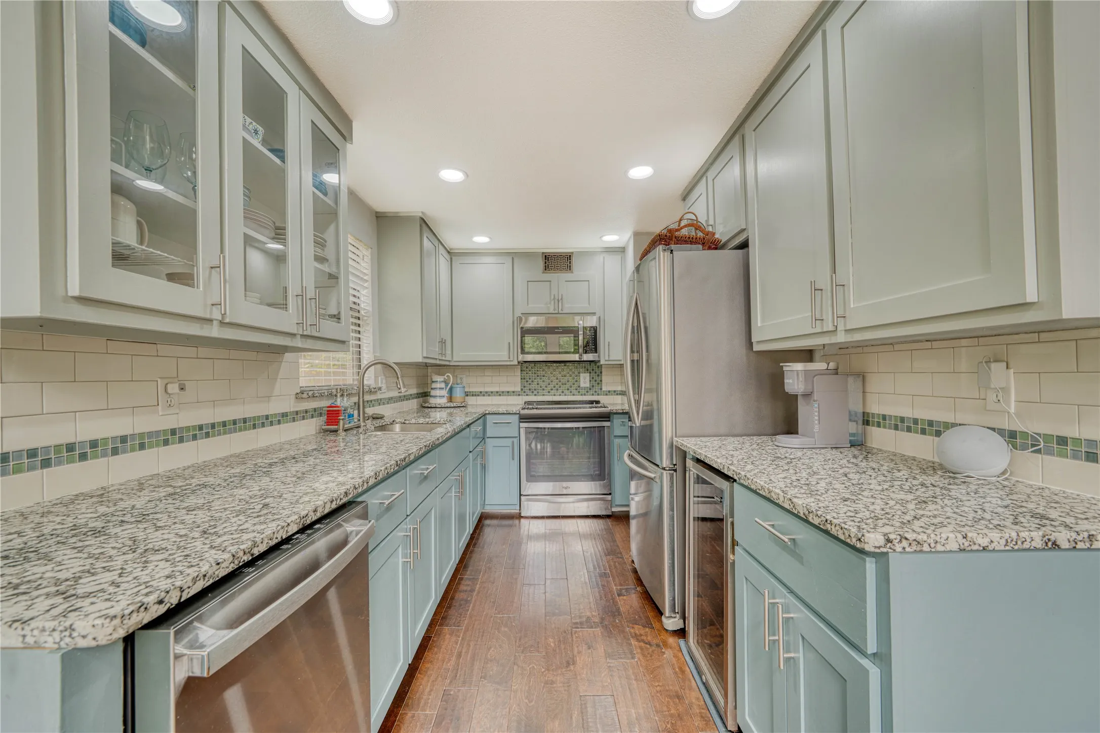 Galley kitchen featuring granite countertops, wood-finish flooring, recessed lighting, stainless steel appliances, and glass-front upper cabinetry