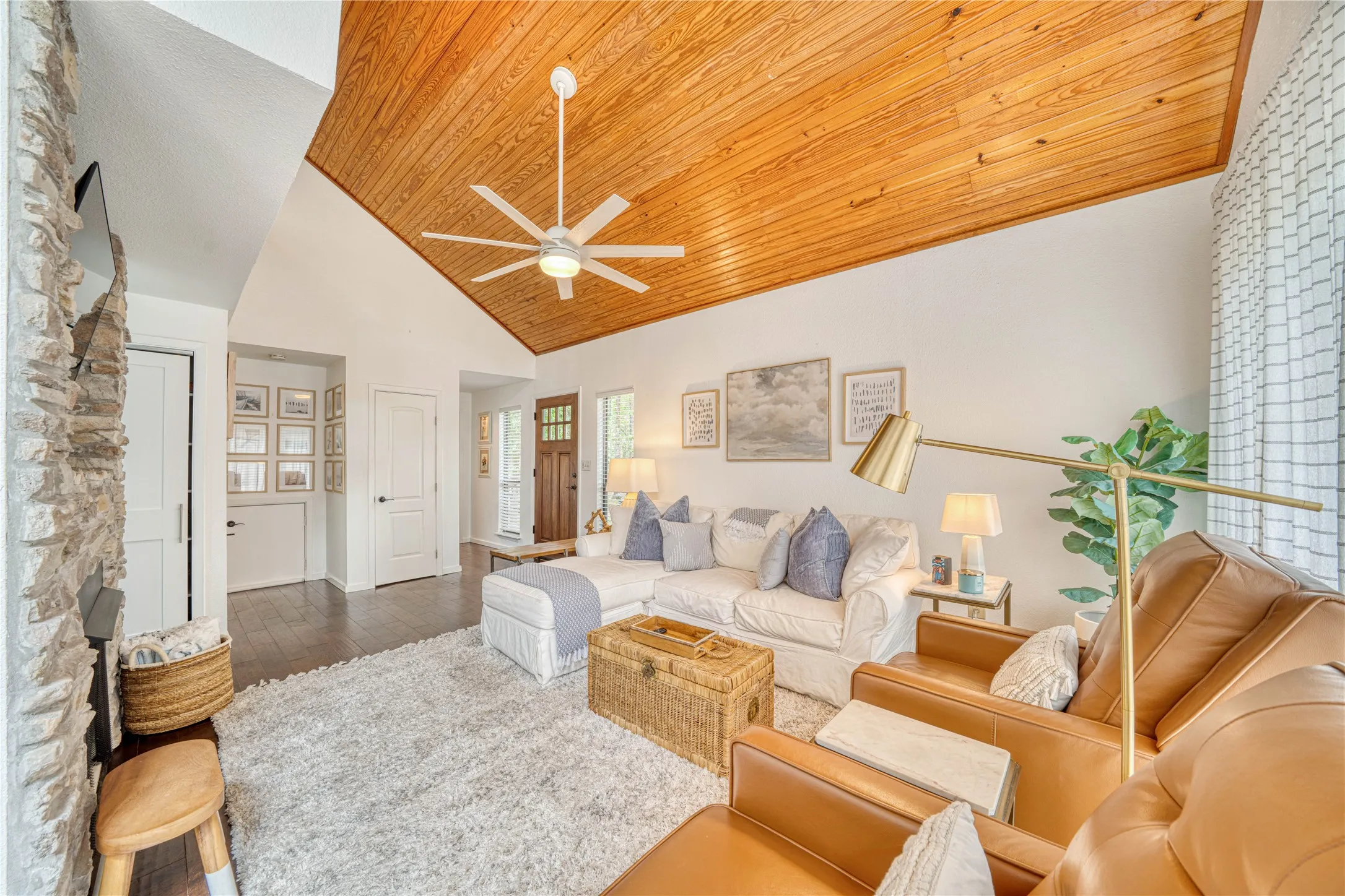 Vaulted ceiling with wood-finish paneling, stone-clad fireplace, dark wood-finish flooring, white paneled doors, and a decorative front entry door