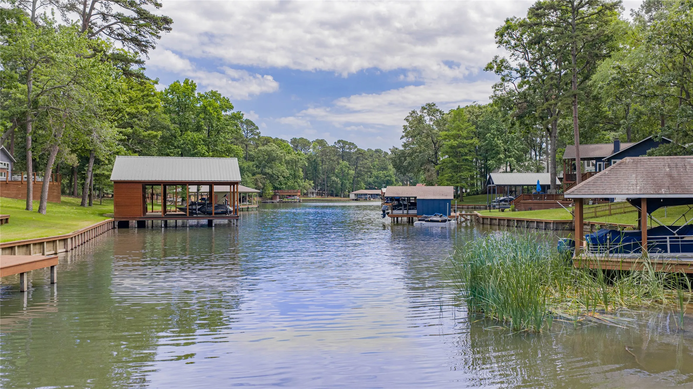 Waterfront property featuring a private boat dock with covered slip, lush green landscaping, and mature trees lining the shore