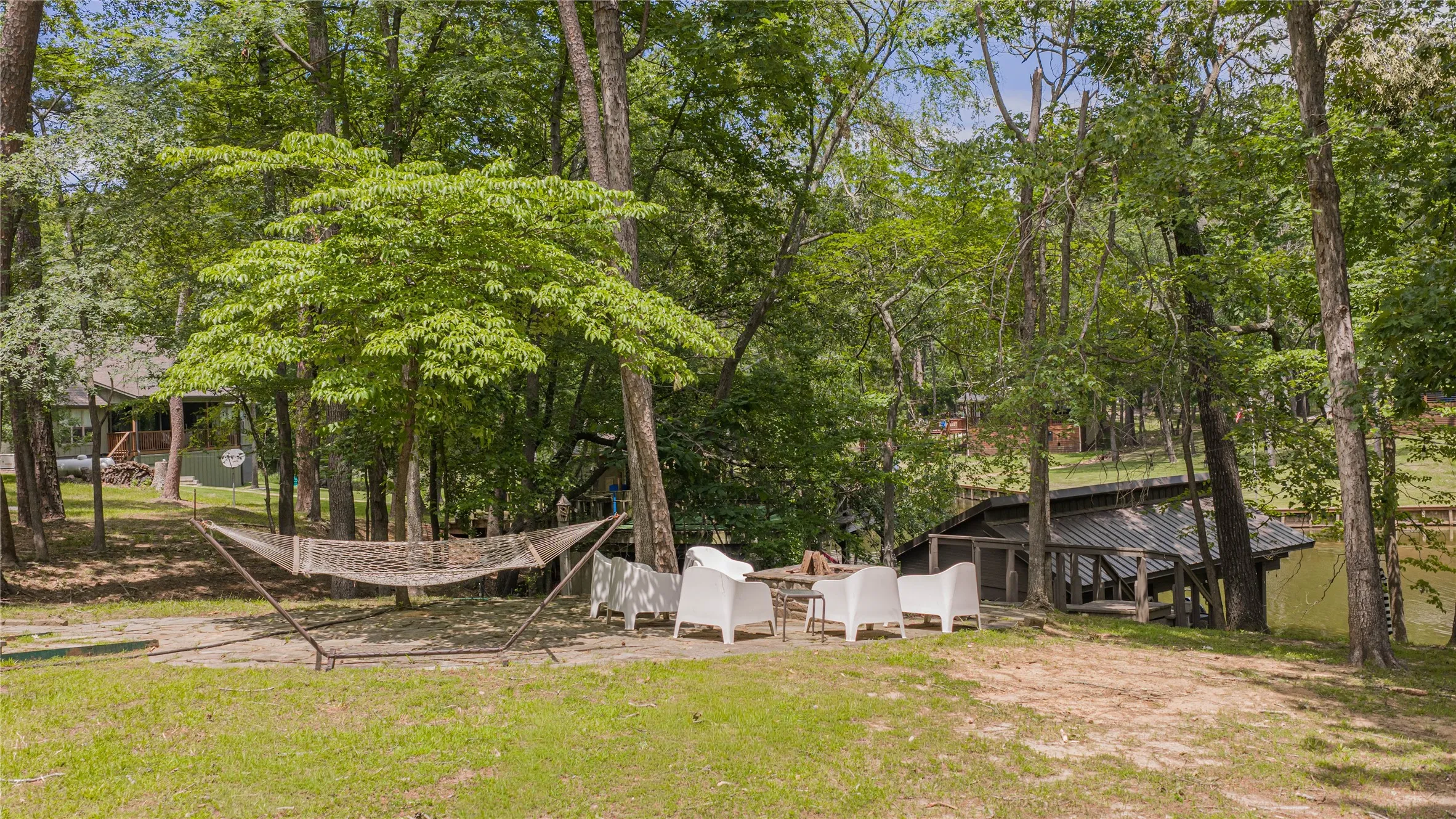 Grassed outdoor area featuring a stone patio, mature trees, and a visible boat house with a metal roof