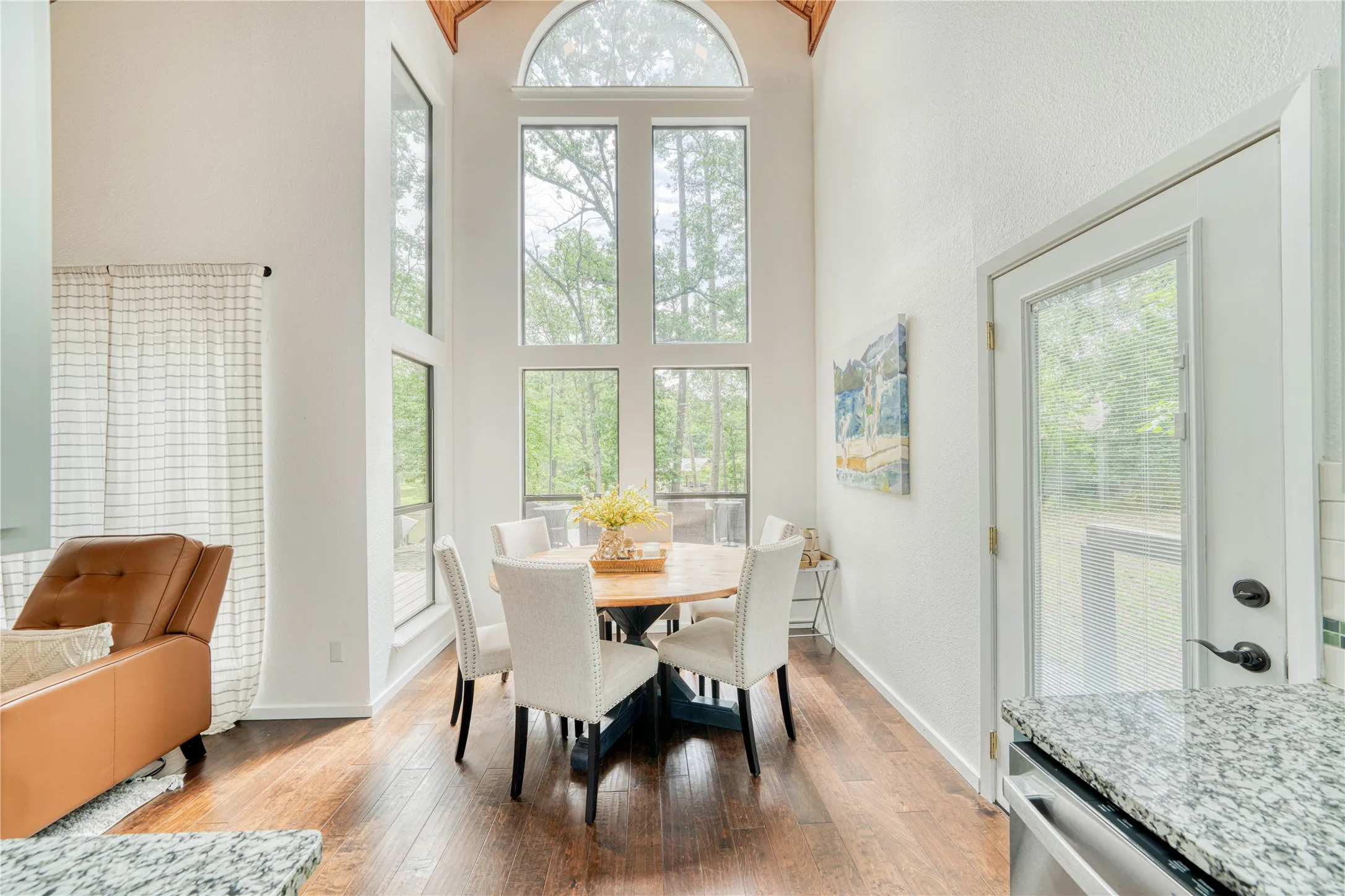 Dining area featuring a vaulted ceiling with exposed wood beams, extensive floor-to-ceiling windows, wood-finish flooring, and a glass-paneled exterior door