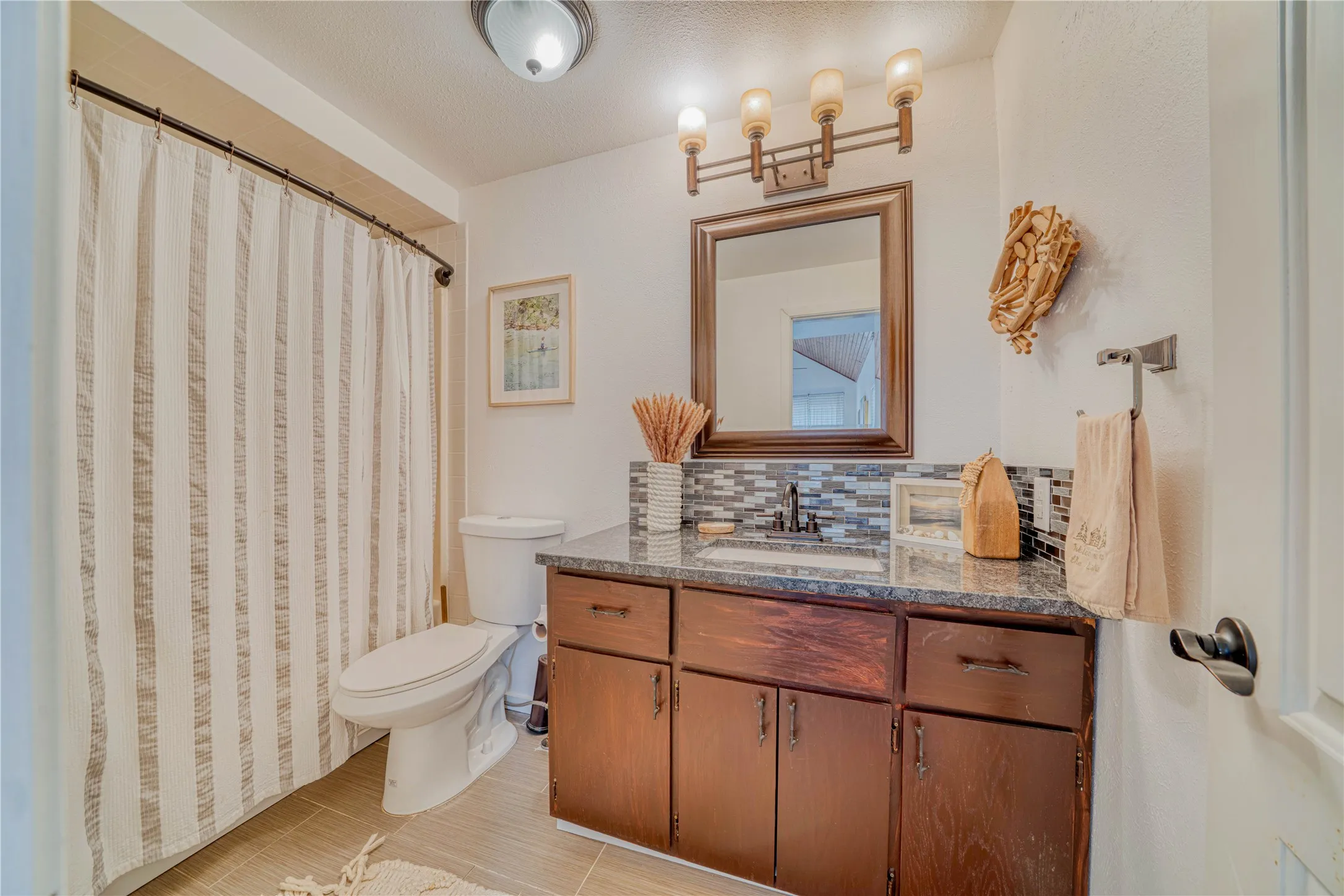 Bathroom featuring a vanity with a dark wood-finish cabinet, stone-finish countertop, and mosaic tile backsplash