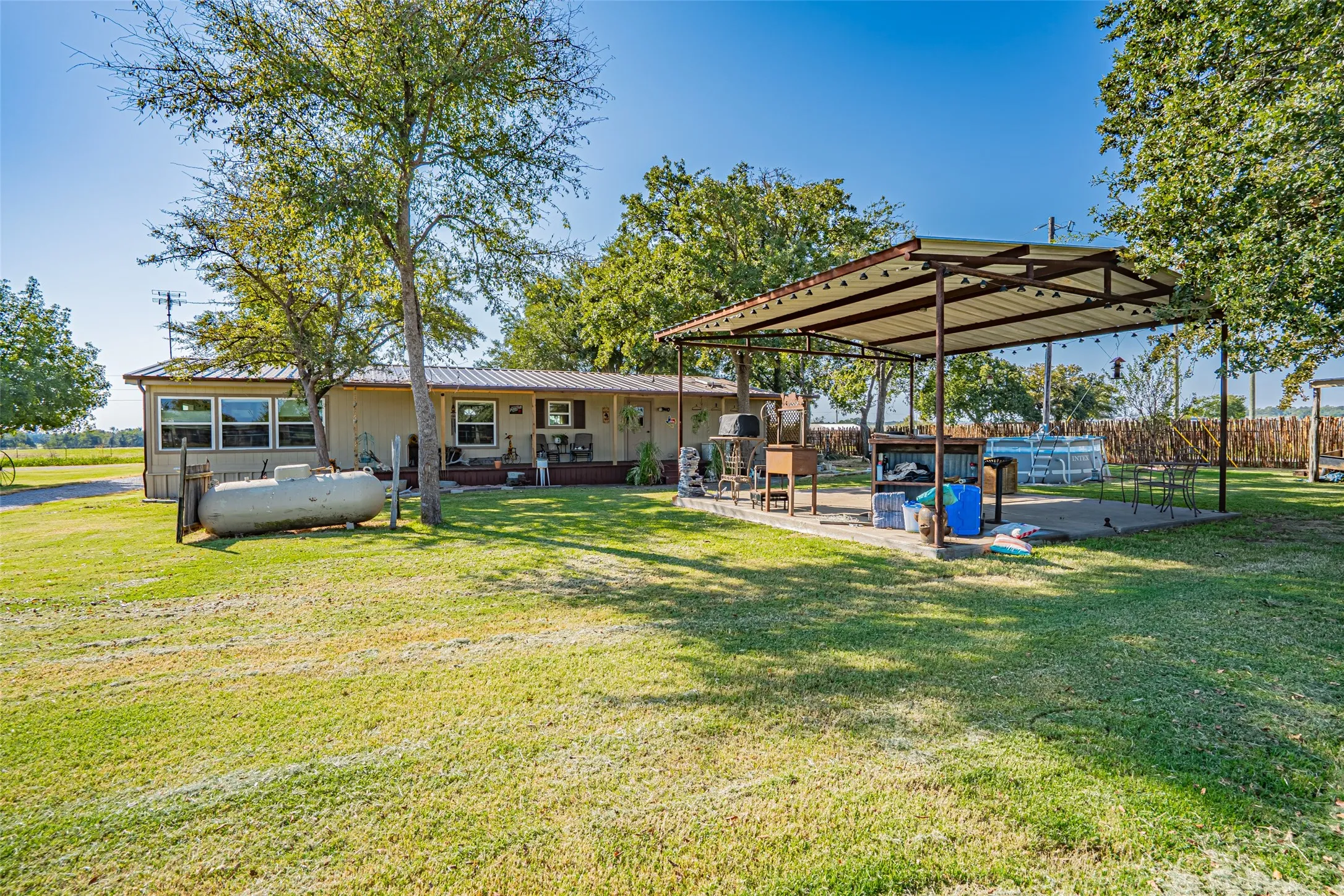 Back of property with a metal roof, a patio, and tree covered back yard. Pool has been removed.