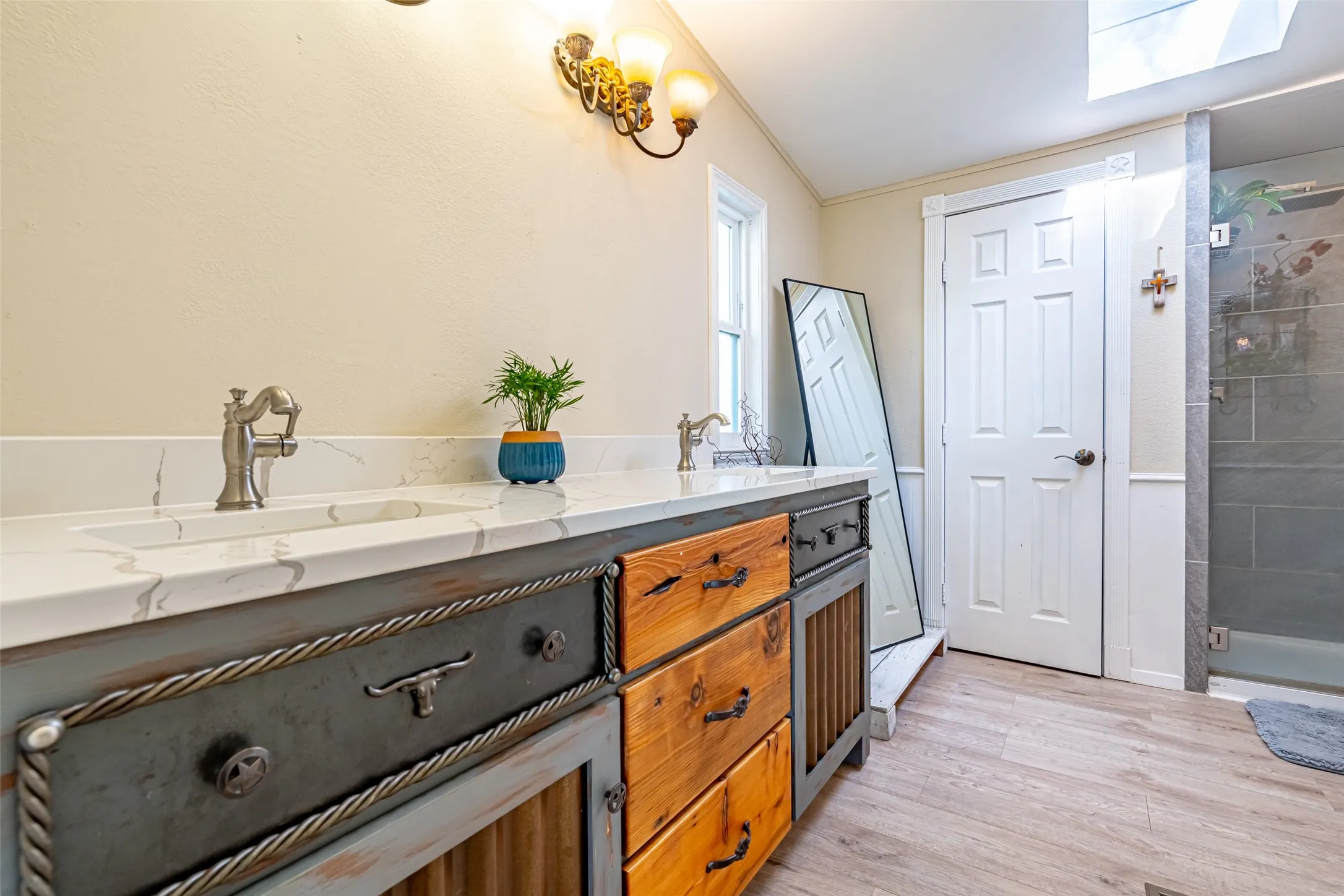 Bathroom with double vanity, a walk-in shower, wood-style flooring, a skylight, and crown molding.