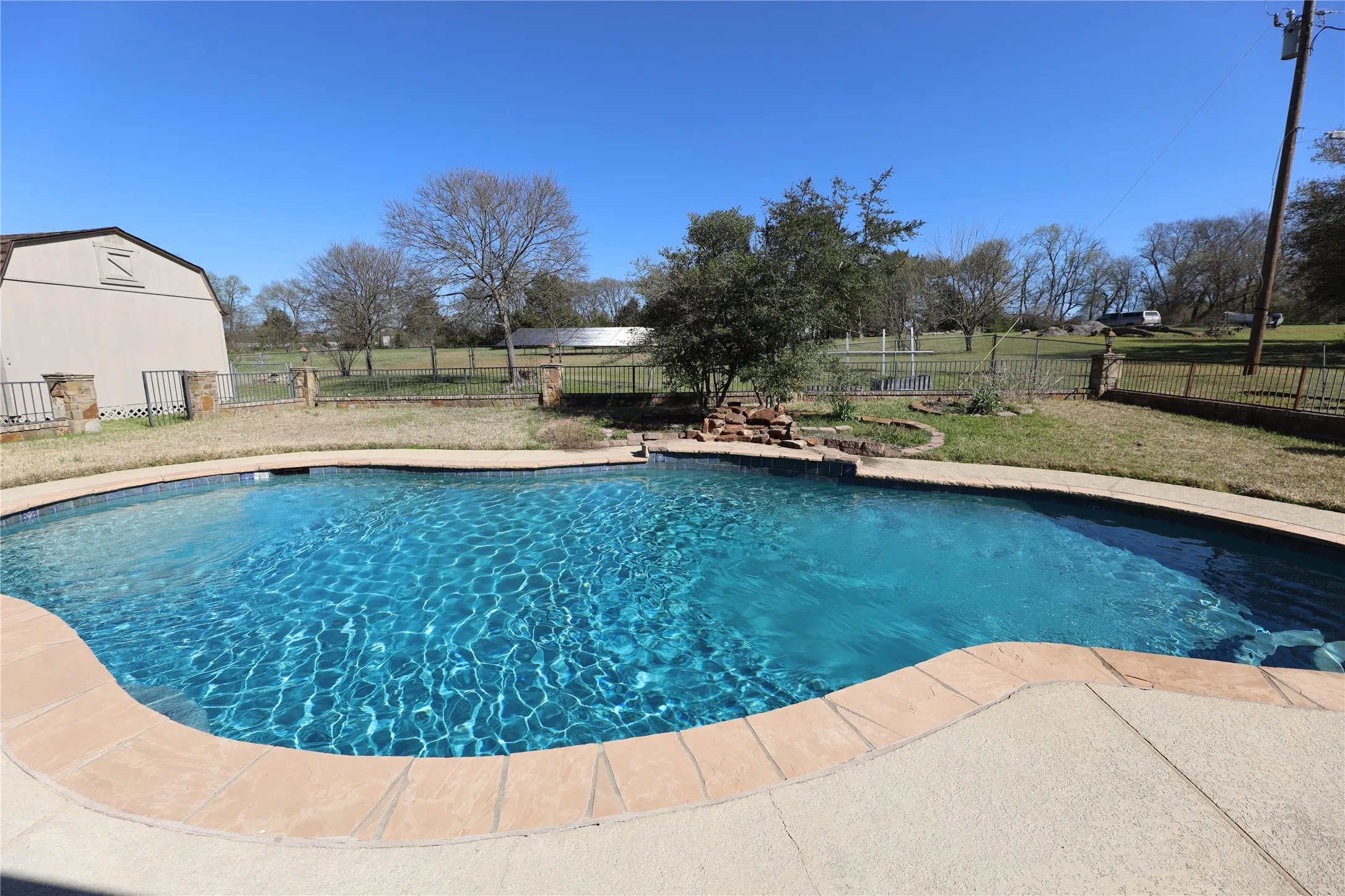 Freeform swimming pool with stone coping, surrounded by a concrete deck
