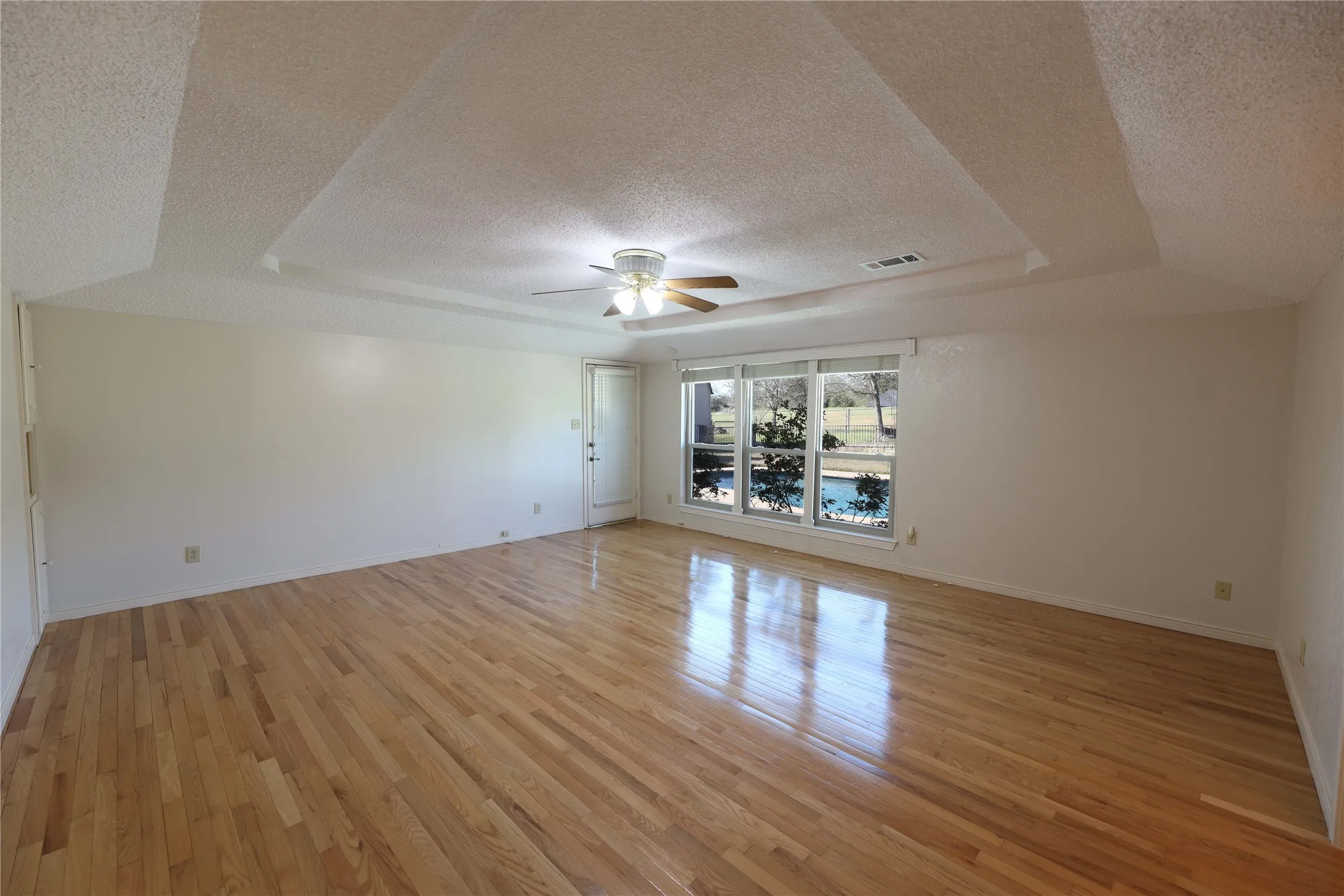 Spacious room featuring wood-finish flooring and a tray ceiling with a ceiling fan