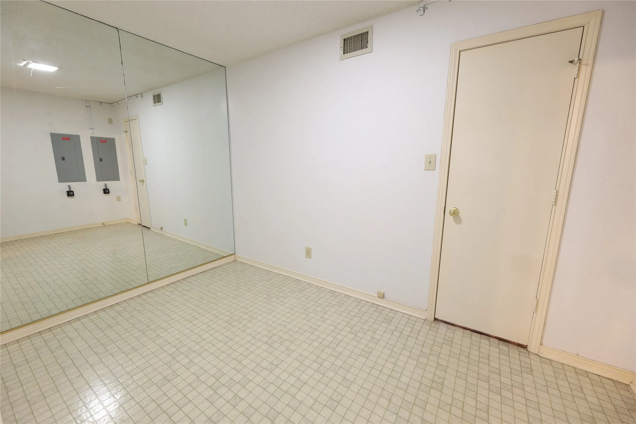 Room featuring a full wall mirror, white painted walls, and light-toned tile flooring