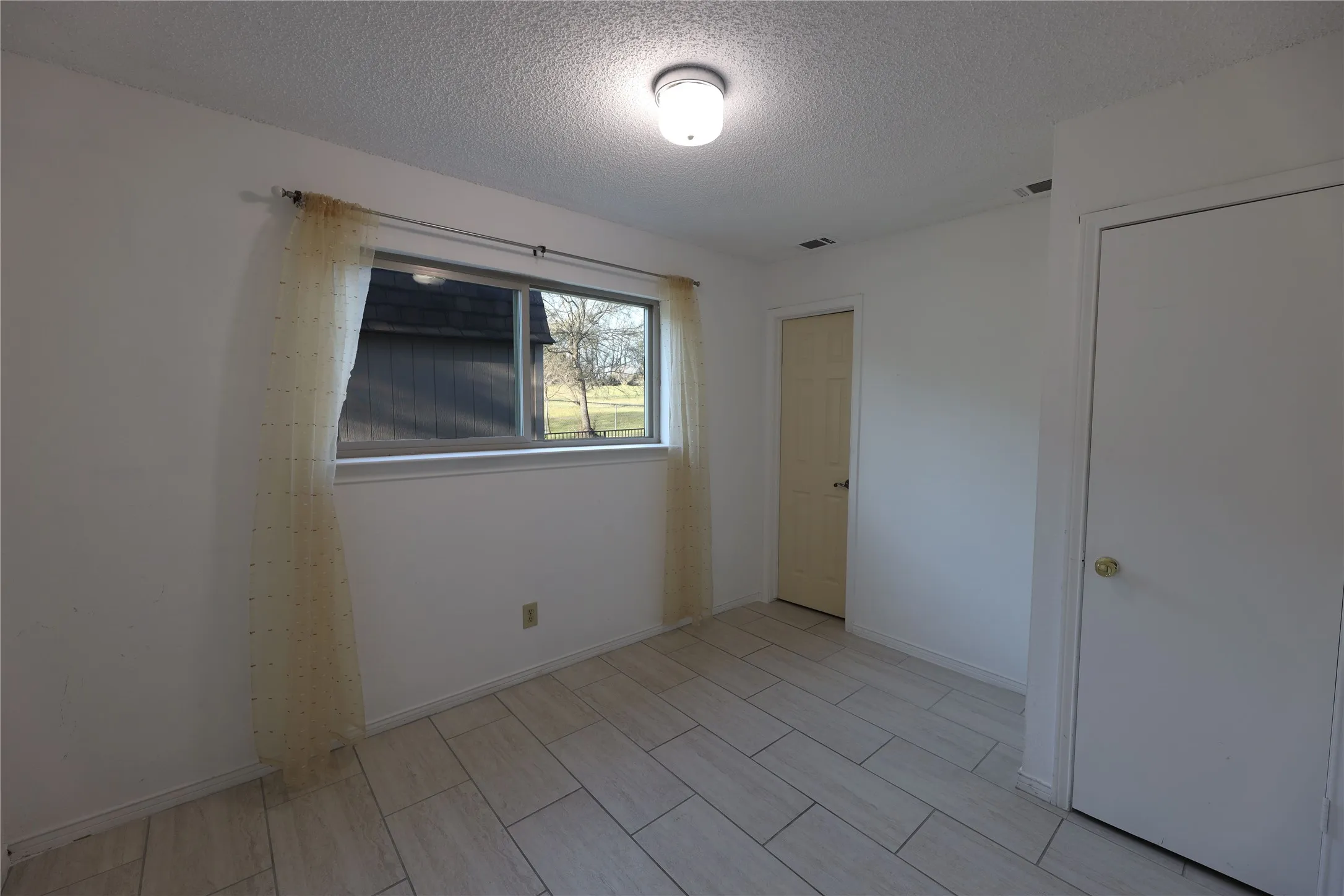 Room featuring light-toned tile flooring, a window with exterior views, and two interior doors