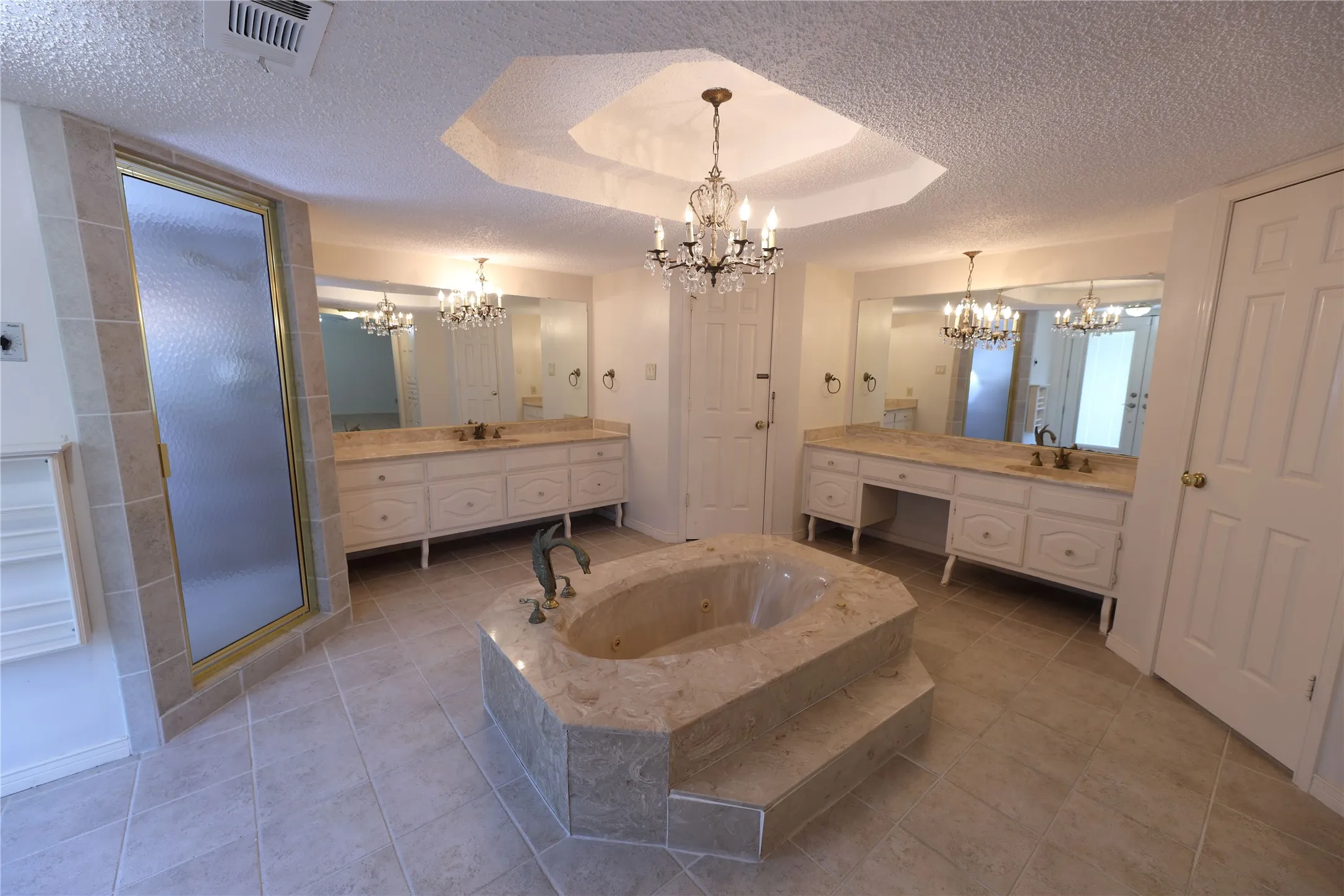 Octagonal jetted tub with tiled surround, dual vanities with integrated sinks, framed mirrors, and a glass-enclosed shower