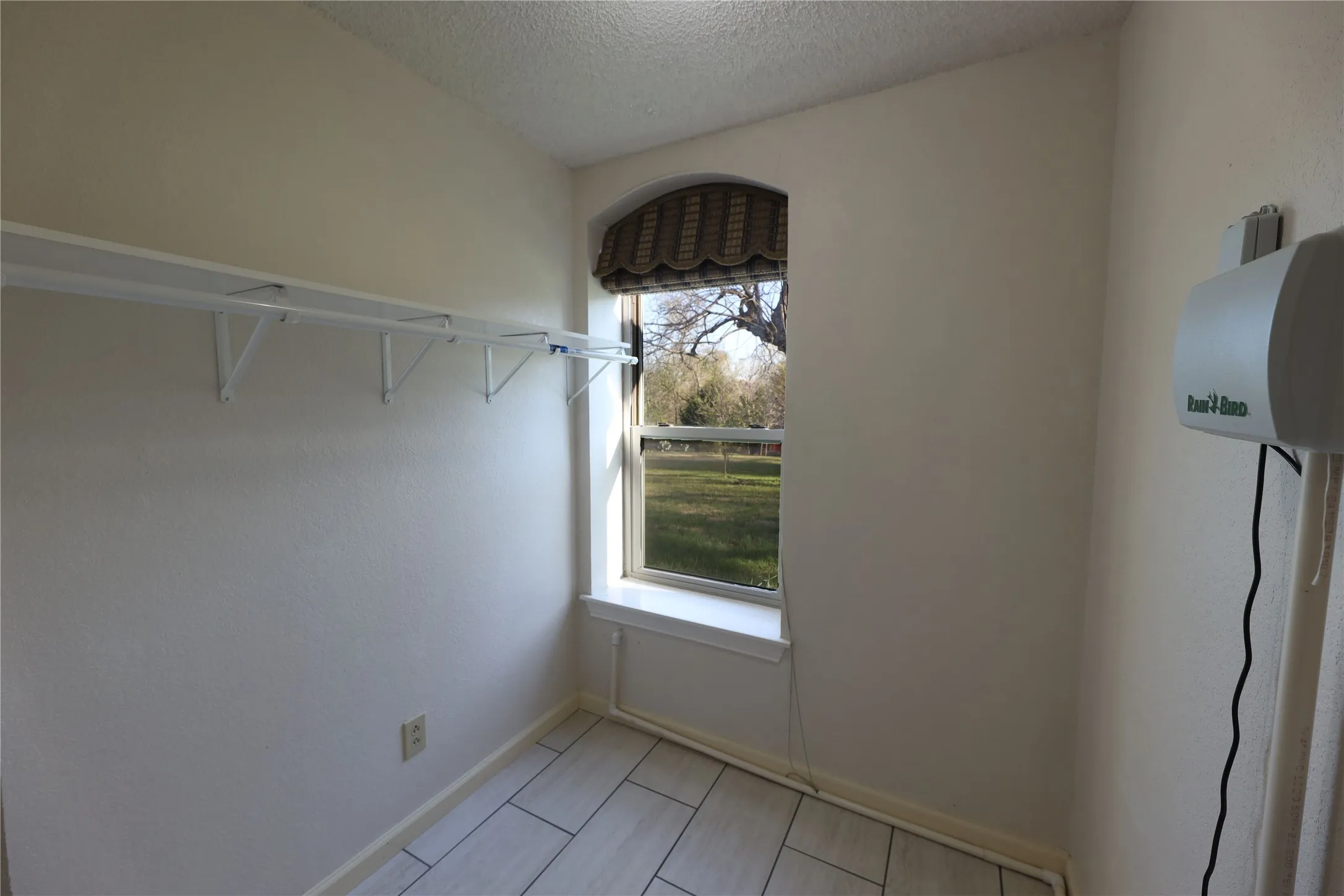 Compact utility space featuring a rectangular window with an arched top, tile flooring, and wall-mounted shelving