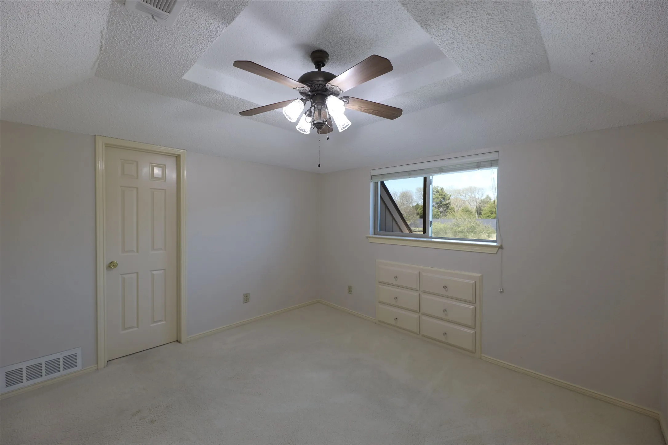 Bedroom featuring a ceiling fan with light fixture, textured ceiling, a built-in window seat with drawers, and carpeted flooring