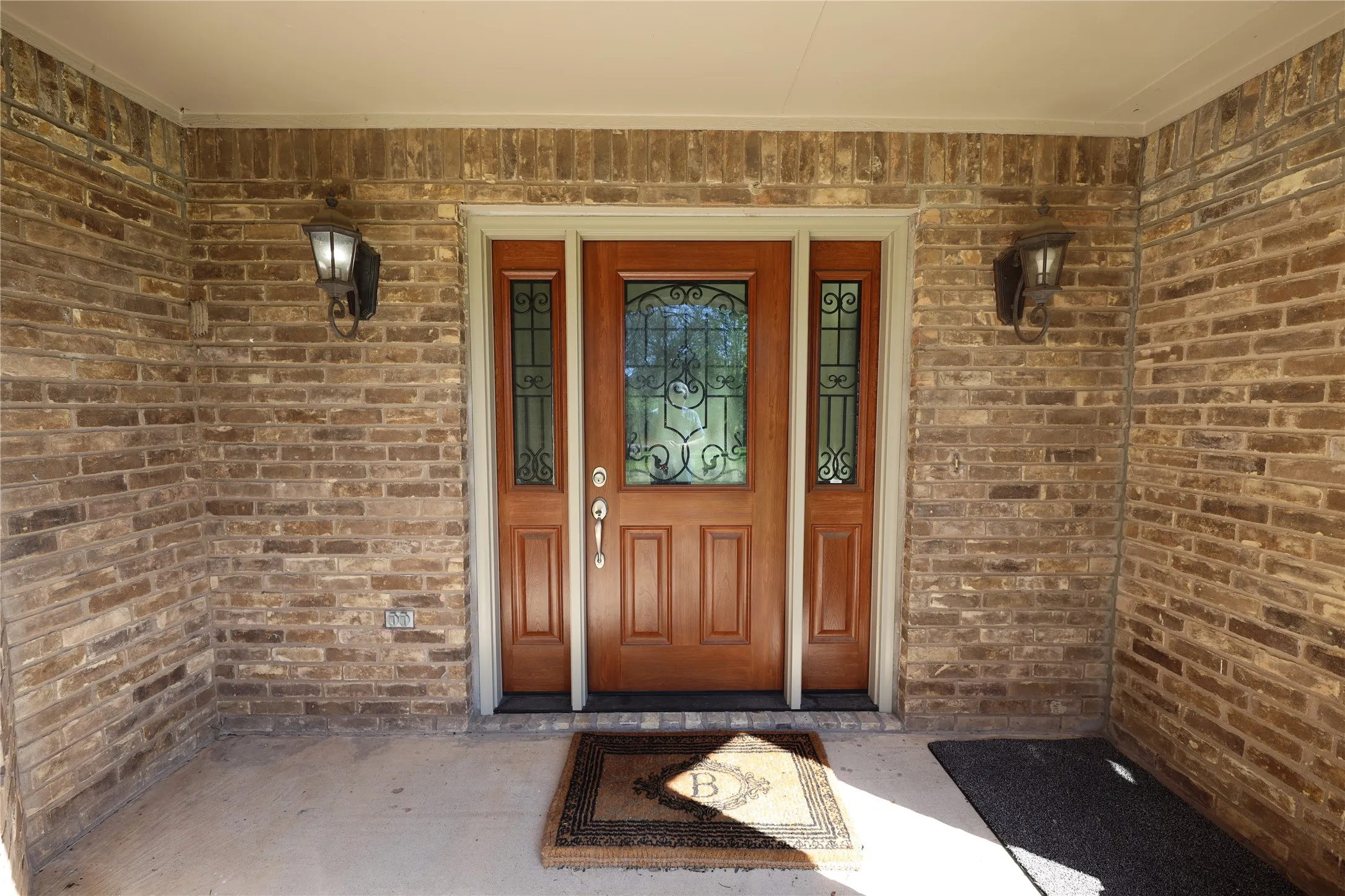Recessed entry featuring a wood-paneled door with decorative glass inserts, flanked by matching sidelights and two exterior sconces