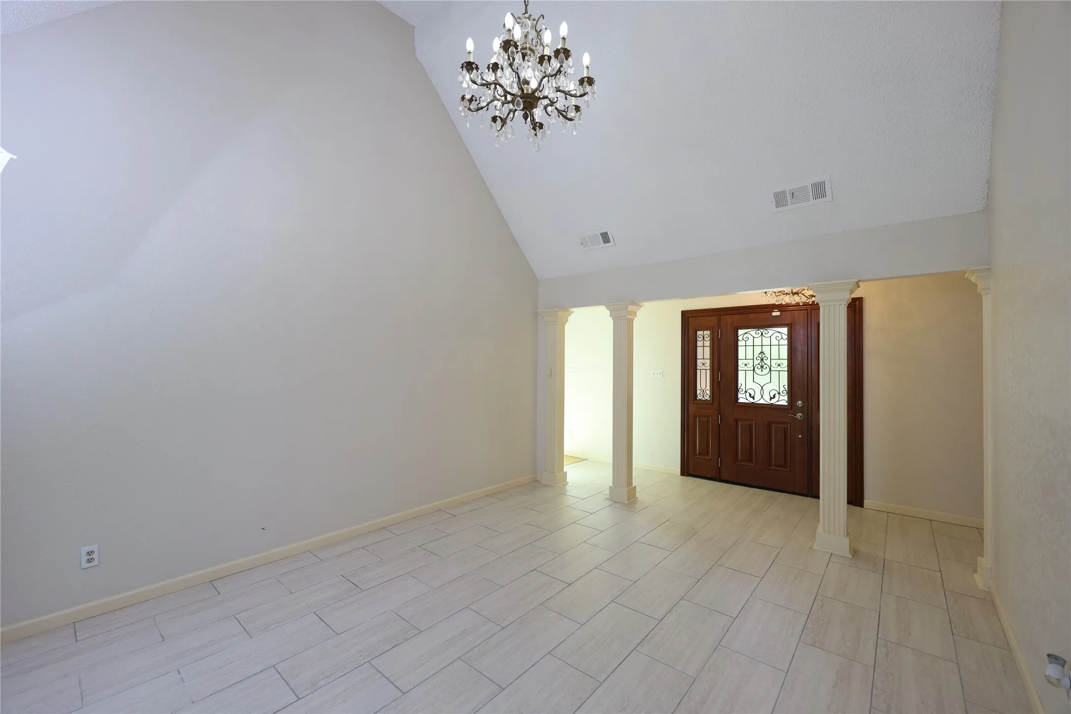 Foyer featuring a double wood entry door with decorative glass inserts, vaulted ceiling, chandelier, and light-toned tile flooring