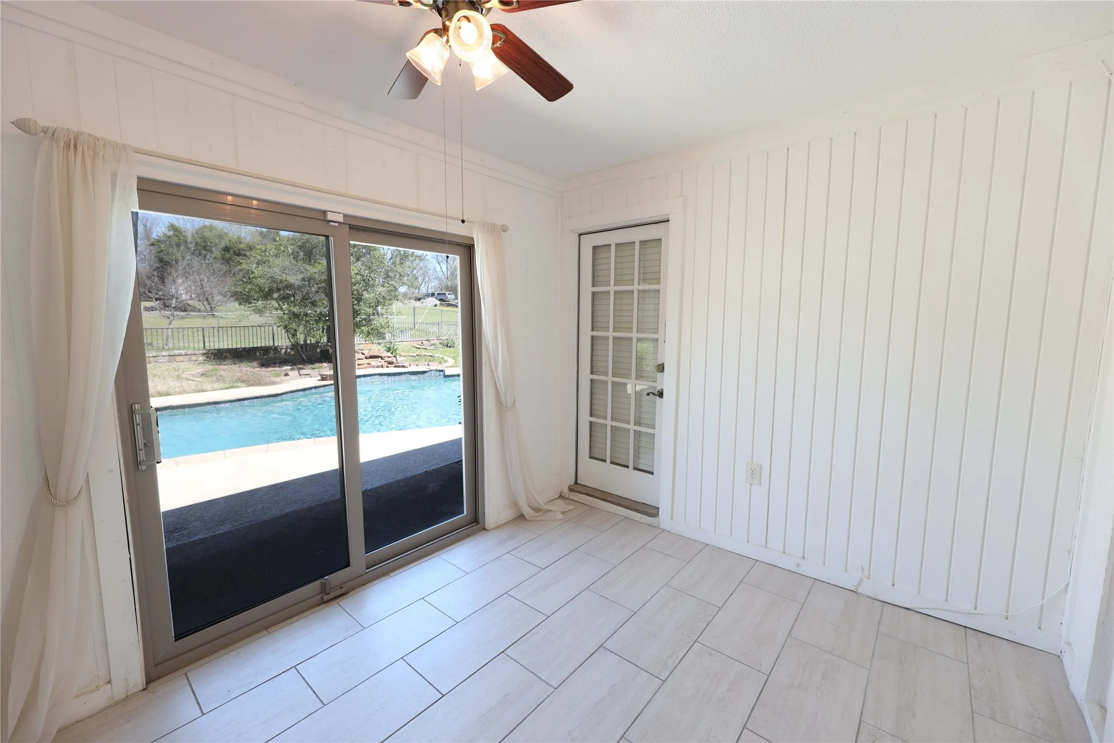 Room featuring light-toned plank-style flooring, white vertical paneled walls, and a ceiling fan with integrated lighting