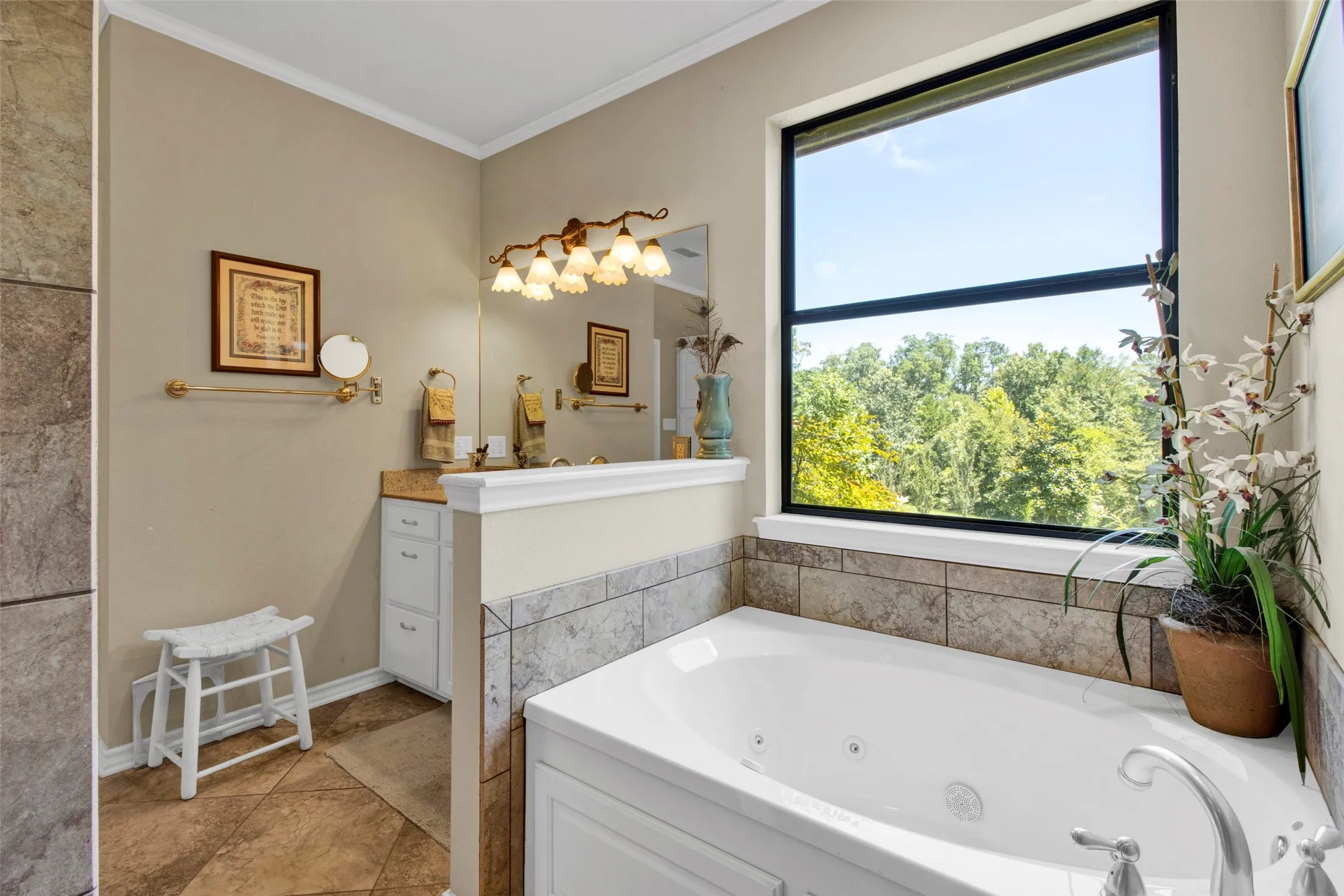 Soaking tub with tile surround, large picture window, double vanity with integrated sinks and a brass-finish light fixture, and tile flooring