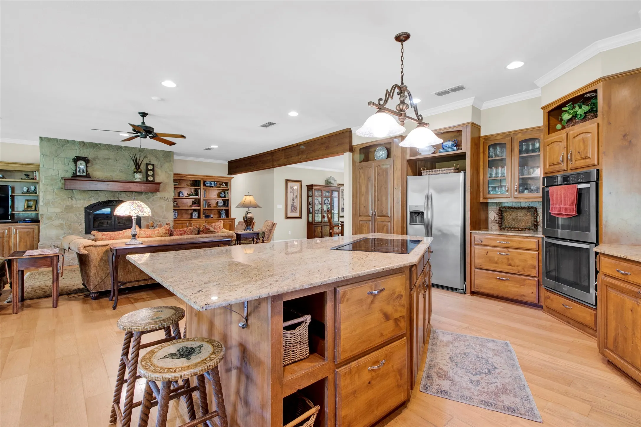 Spacious kitchen featuring a functional island with electric cooktop and pendant lighting, wood cabinetry, granite countertops, and storage - opens to Living Room